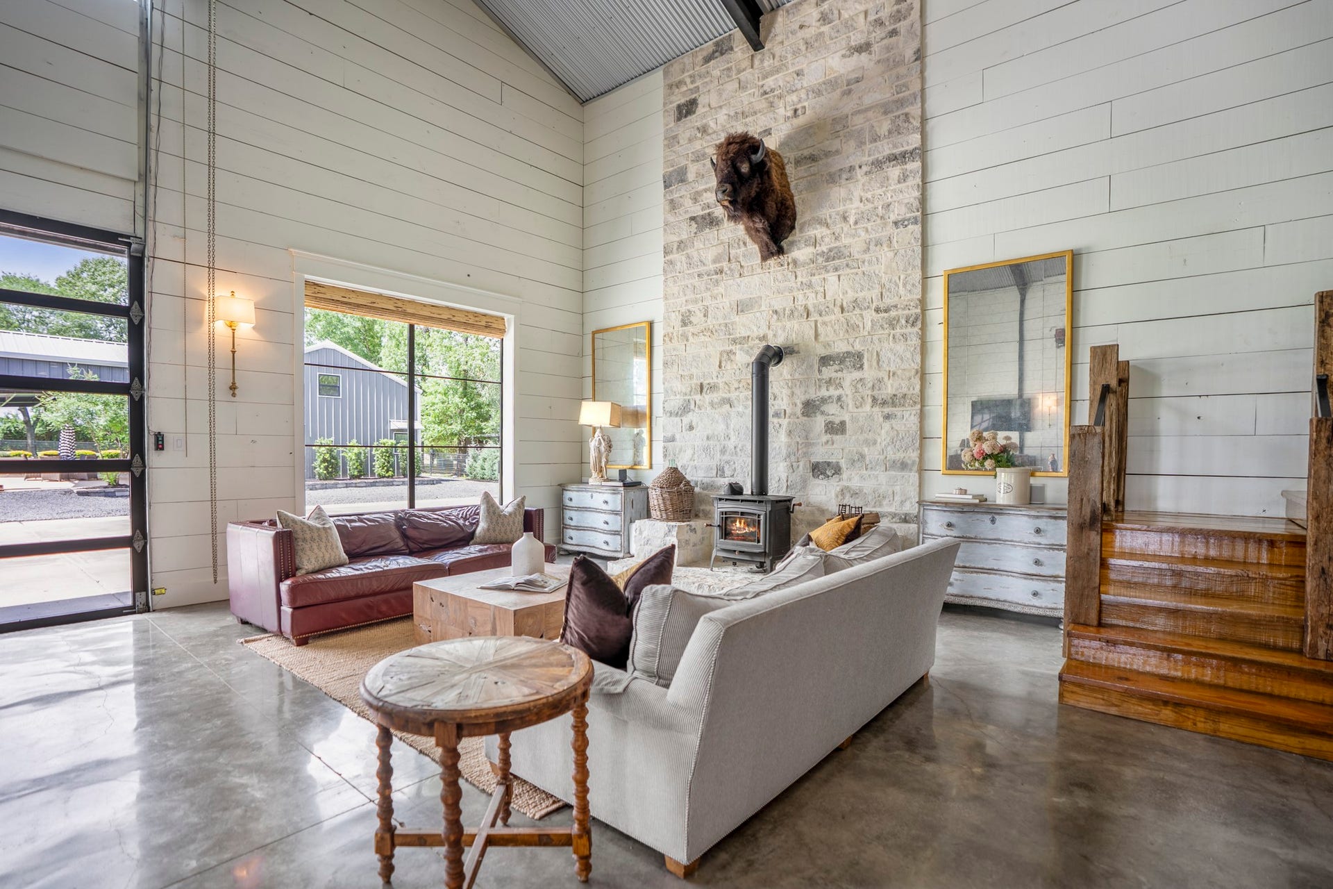 Dramatic living room showcasing a floor-to-ceiling stone fireplace with wood-burning stove, expansive remote-controlled glass bay doors and concrete floors,