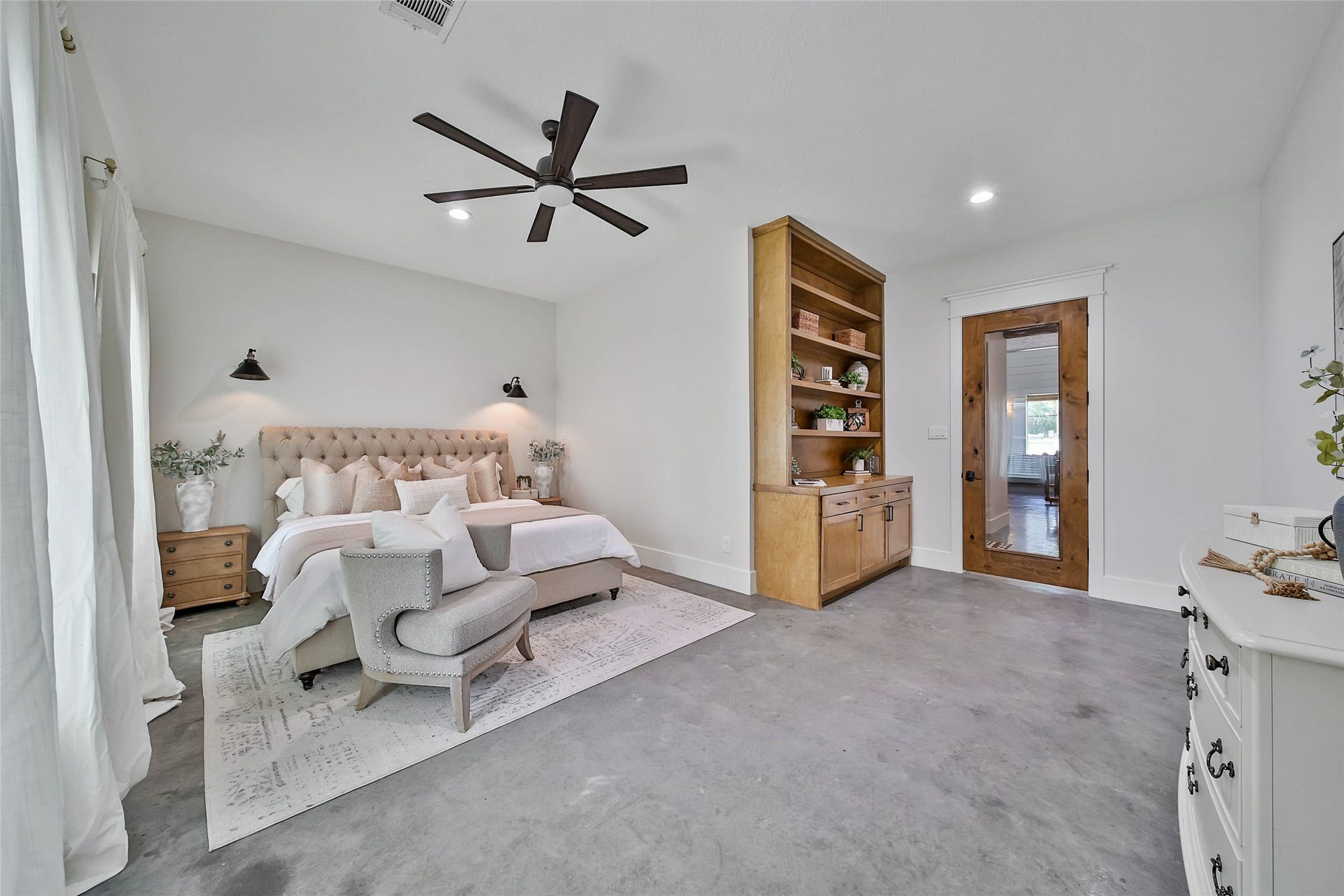 Spacious downstairs secondary bedroom featuring concrete floors, abundant natural light, recessed lighting, designer ceiling fan, custom built-in shelving and cabinetry, plus convenient access to a beautifully appointed full bath.