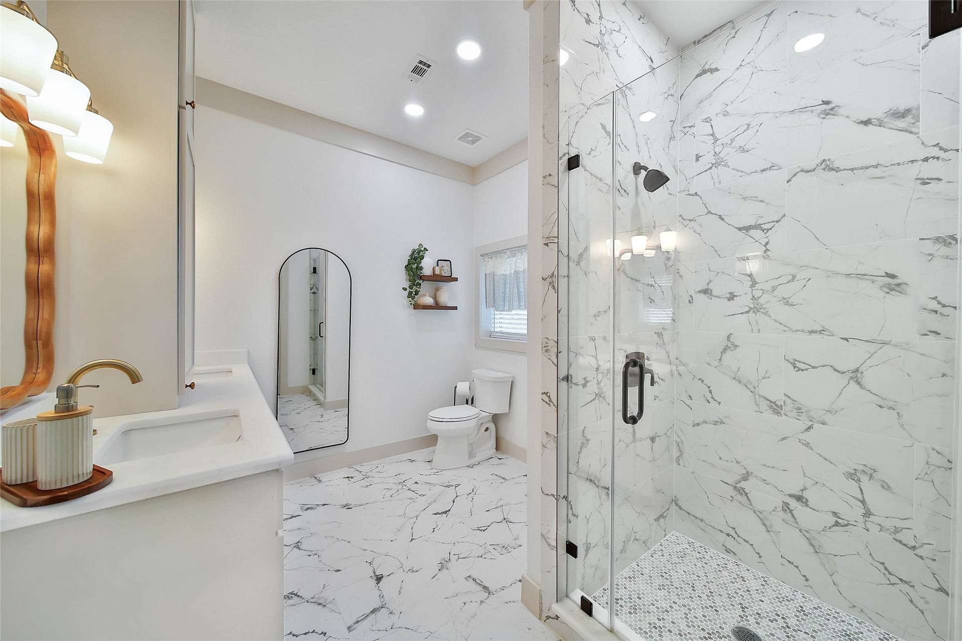 Spa-inspired garage apartment bath features a frameless glass walk-in shower, marble-look tile, quartz vanity and designer finishes throughout.