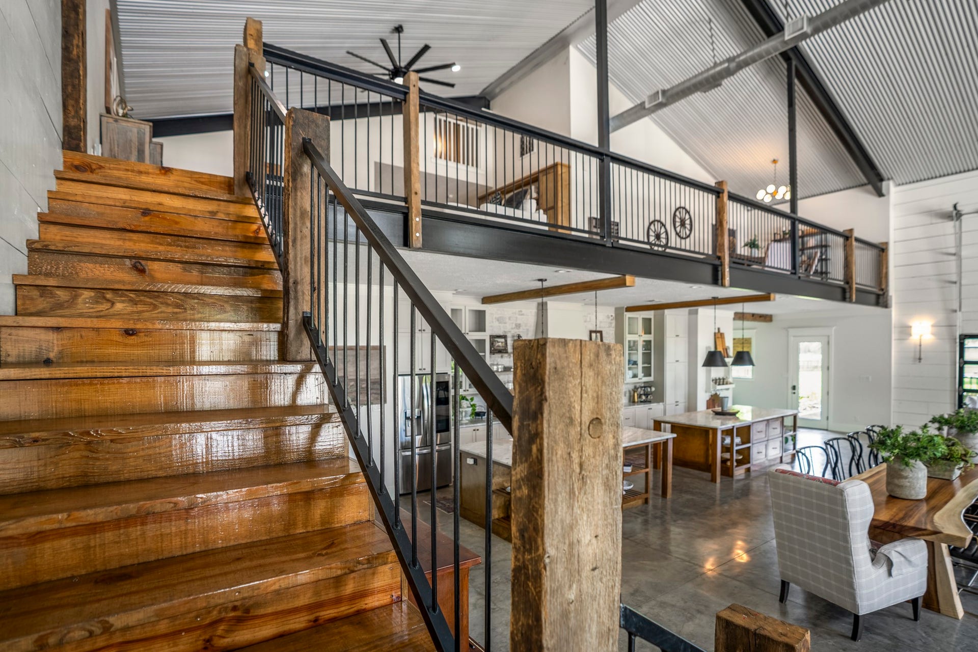 Striking staircase crafted from reclaimed 200-year-old barn wood by Old World Lumber, complemented by exposed steel beams, custom metal balusters, and an expansive open balcony overlooking the dramatic great room below.