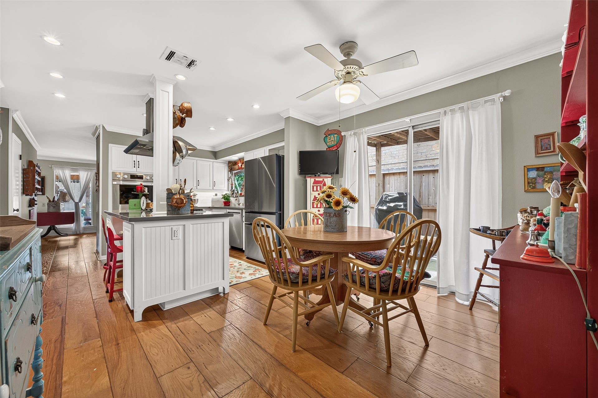 Kitchen and dining area with warm wood flooring, bright white cabinetry, and stainless steel appliances. The cozy dining nook features a round wooden table, perfect for family gatherings, with sliding doors leading to a private patio.