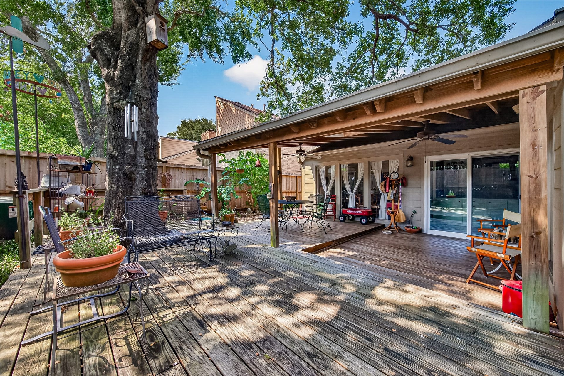 Charming outdoor space featuring a spacious wooden deck, perfect for entertaining, with a covered patio area, mature trees, and cozy seating.