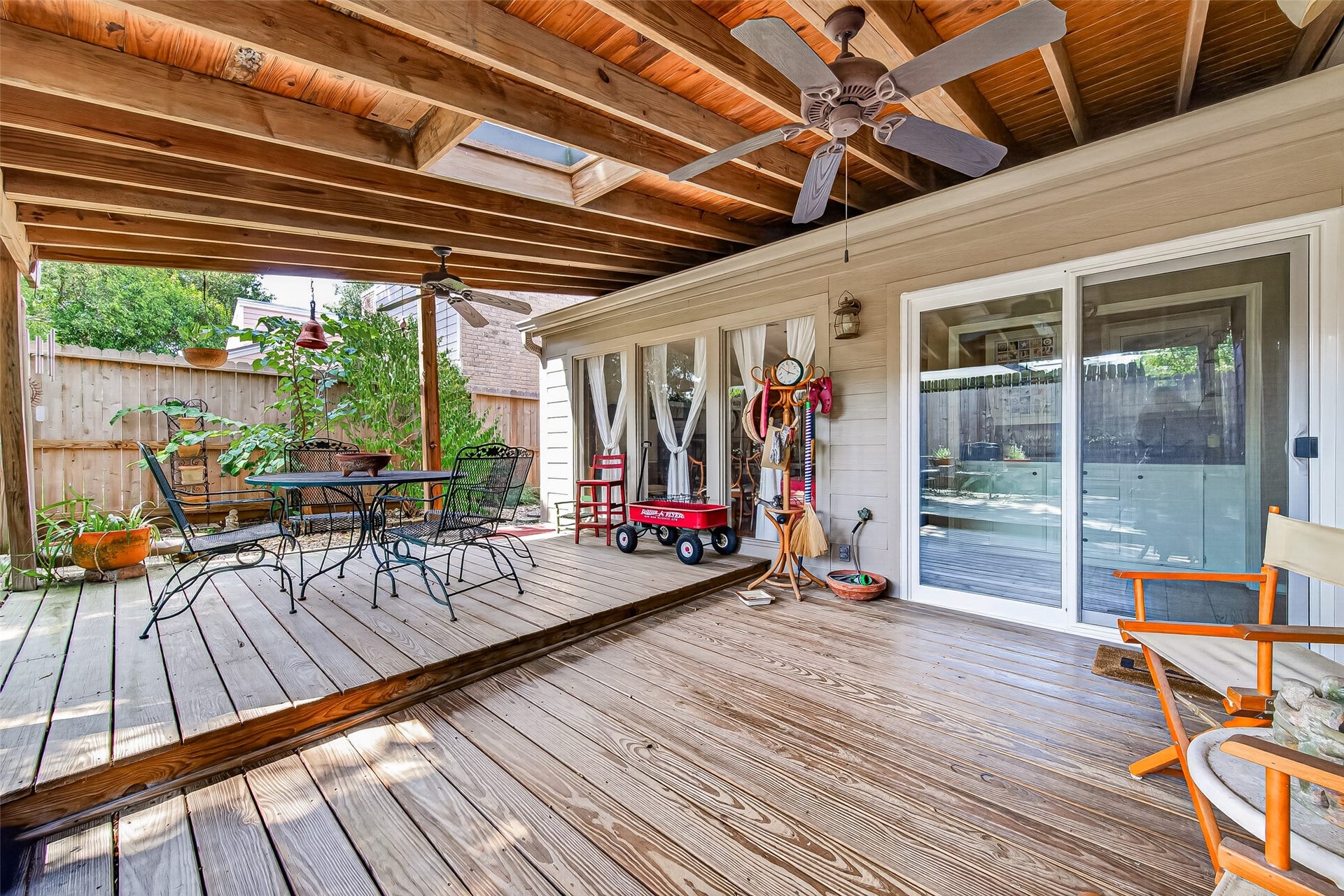 Covered patio with wood decking, ceiling fans, and ample natural light, perfect for outdoor dining and relaxation.