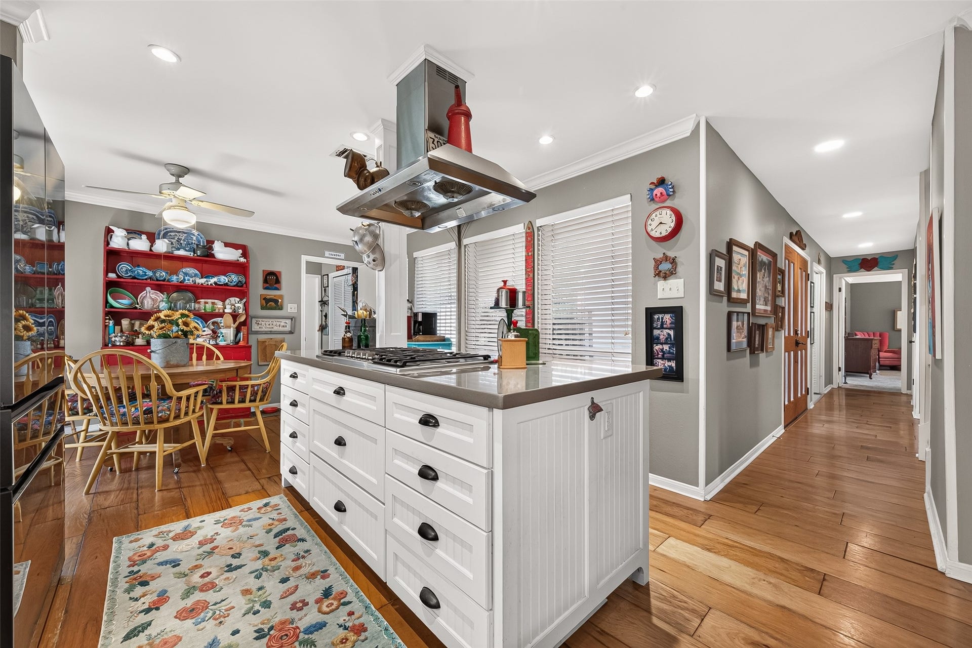 Kitchen with a central island featuring ample drawer storage and cooktop, complemented by natural light from large windows. A cozy dining area with colorful shelving adds a touch of whimsy and warmth to the space.