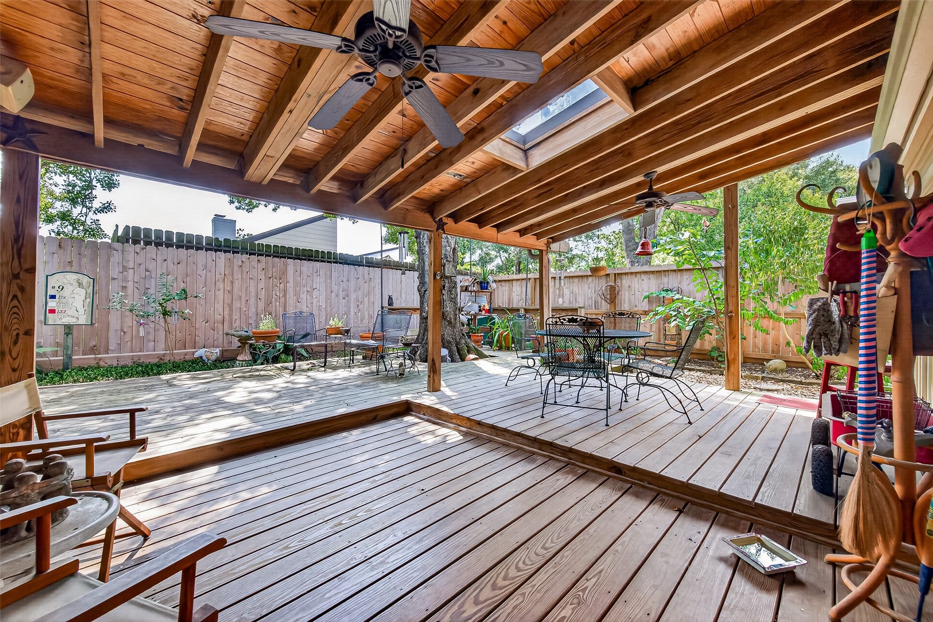 Spacious covered deck with natural wood accents, ceiling fans, and a skylight, perfect for outdoor dining and relaxation amidst a private fenced yard.