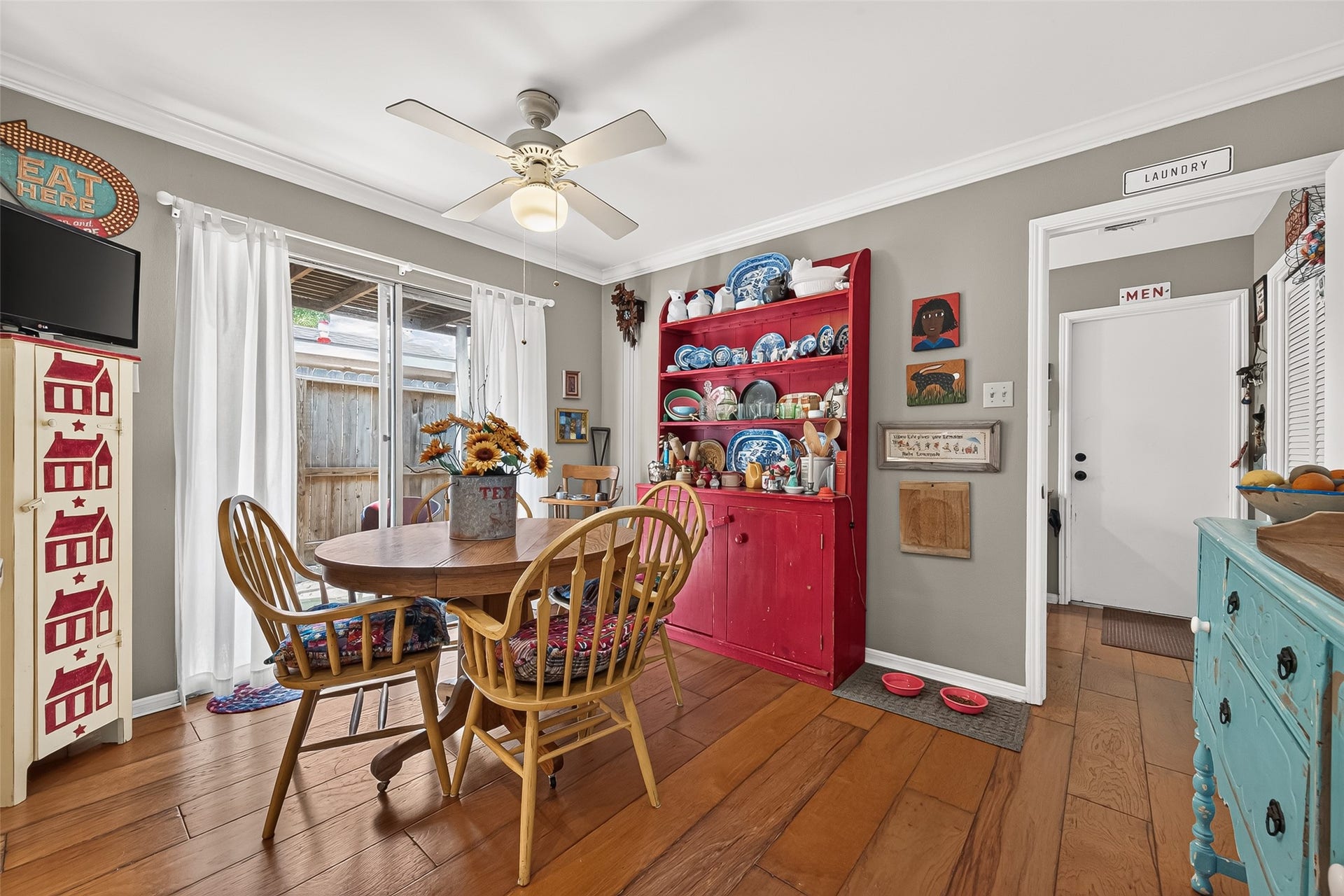 Dining area with warm hardwood floors, featuring a cozy round table and vibrant decor. Natural light pours in through the sliding glass doors, creating an inviting atmosphere perfect for intimate meals.