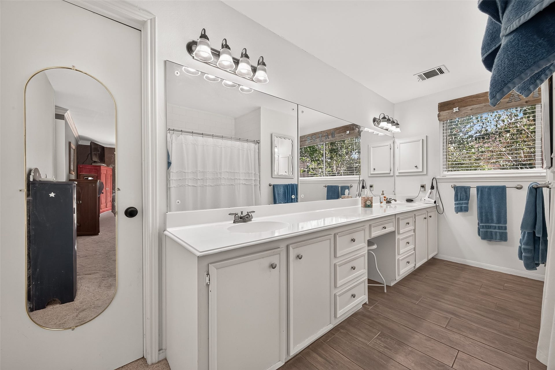 Spacious primary bathroom with dual sinks and a large mirror, offering ample storage and natural light.