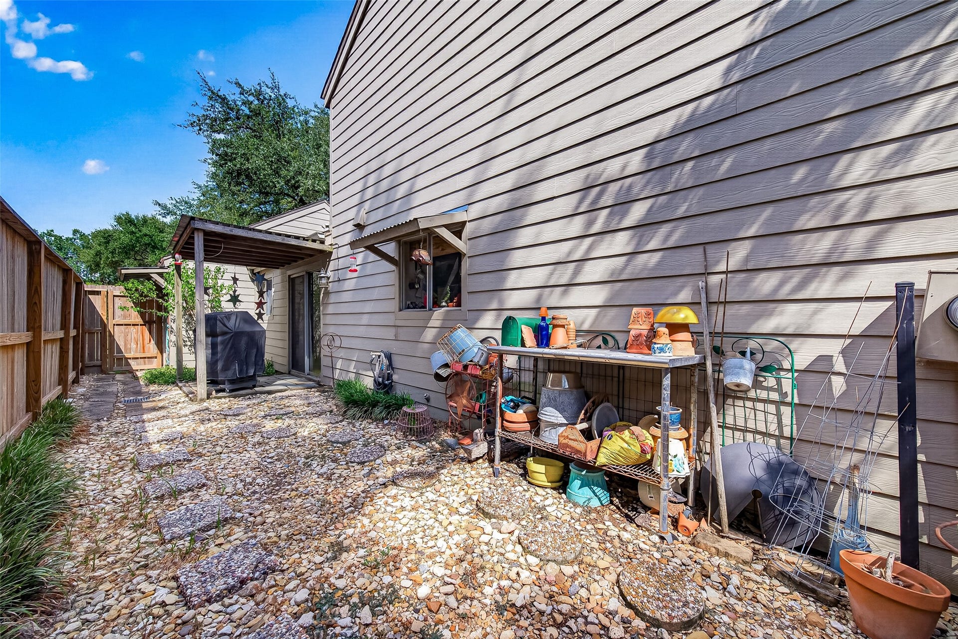 Side yard with a stone path, storage shelving for gardening essentials, and a cozy covered patio area perfect for outdoor relaxation.
