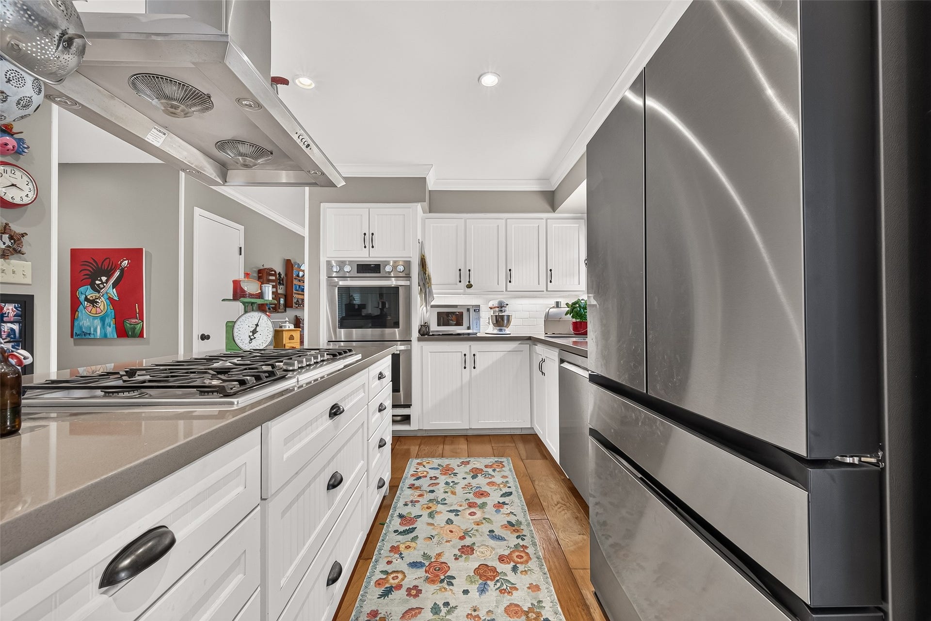 Modern kitchen featuring sleek stainless steel appliances, white cabinetry, and a spacious island with a gas cooktop, all accentuated by warm wood flooring and vibrant decor.
