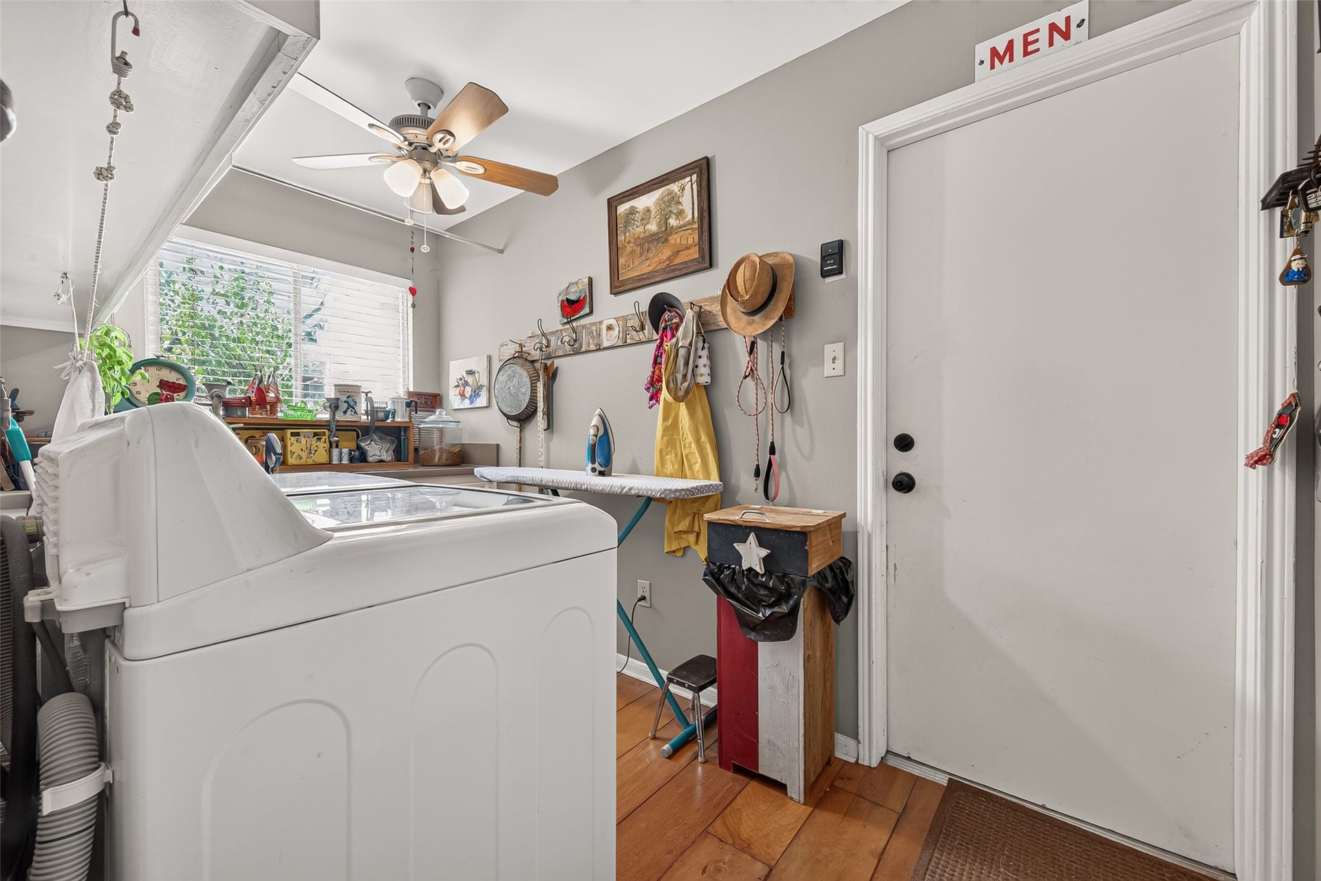 Bright and functional laundry room with ample storage, ironing board, and natural light streaming through a large window, creating an efficient and inviting space. Door leads to garage.