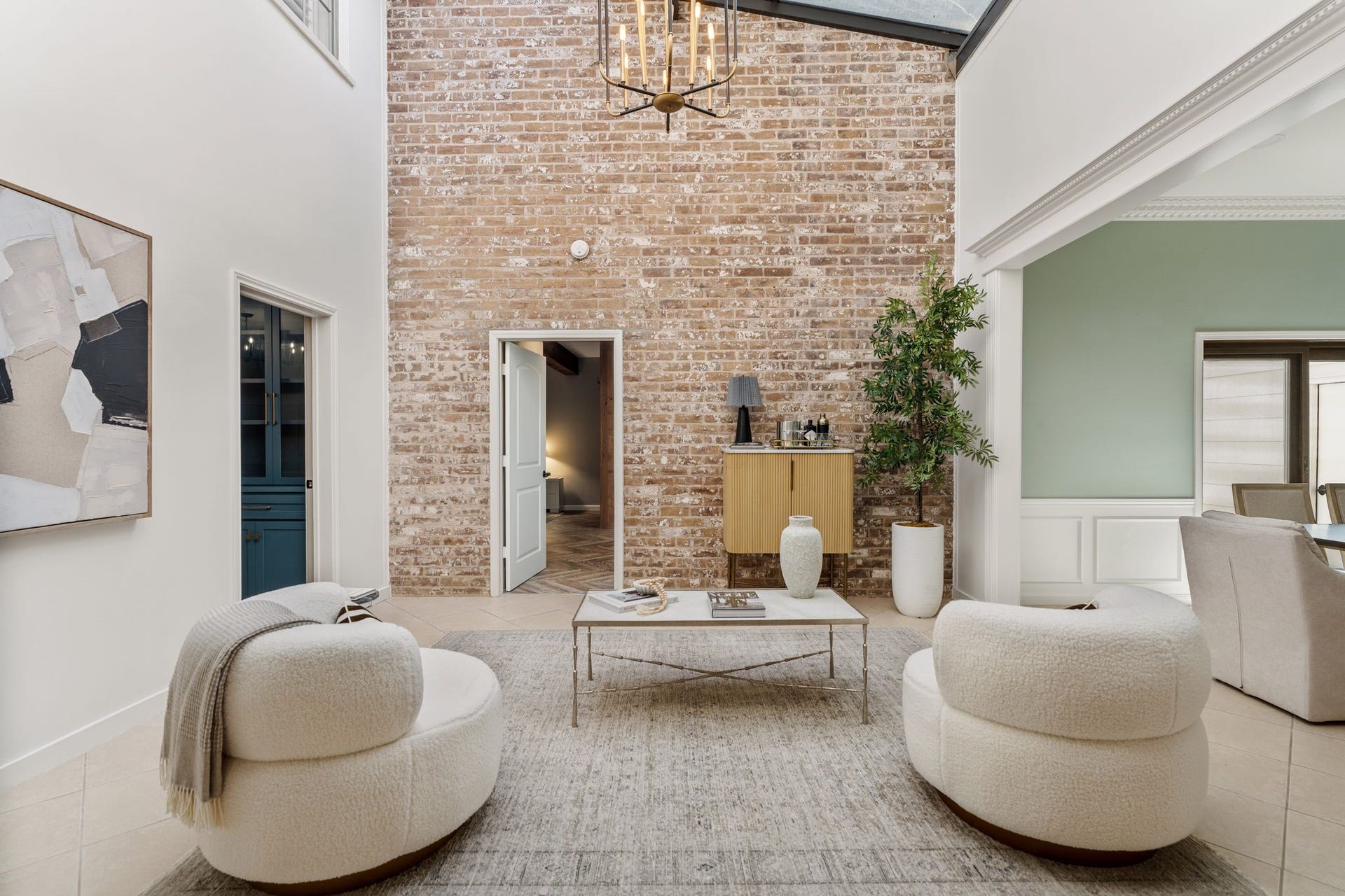 8619 La Fonte Street, Houston, TX 77024 The formal living room features dramatic double-height ceilings, a full-height brick accent wall and an expansive skylight that fills the space with natural light. A decorative gold-and-black light fixture and neutral tile flooring complete the room. The doorway to the left leads to the media room, while the doorway straight ahead provides access to the primary suite.