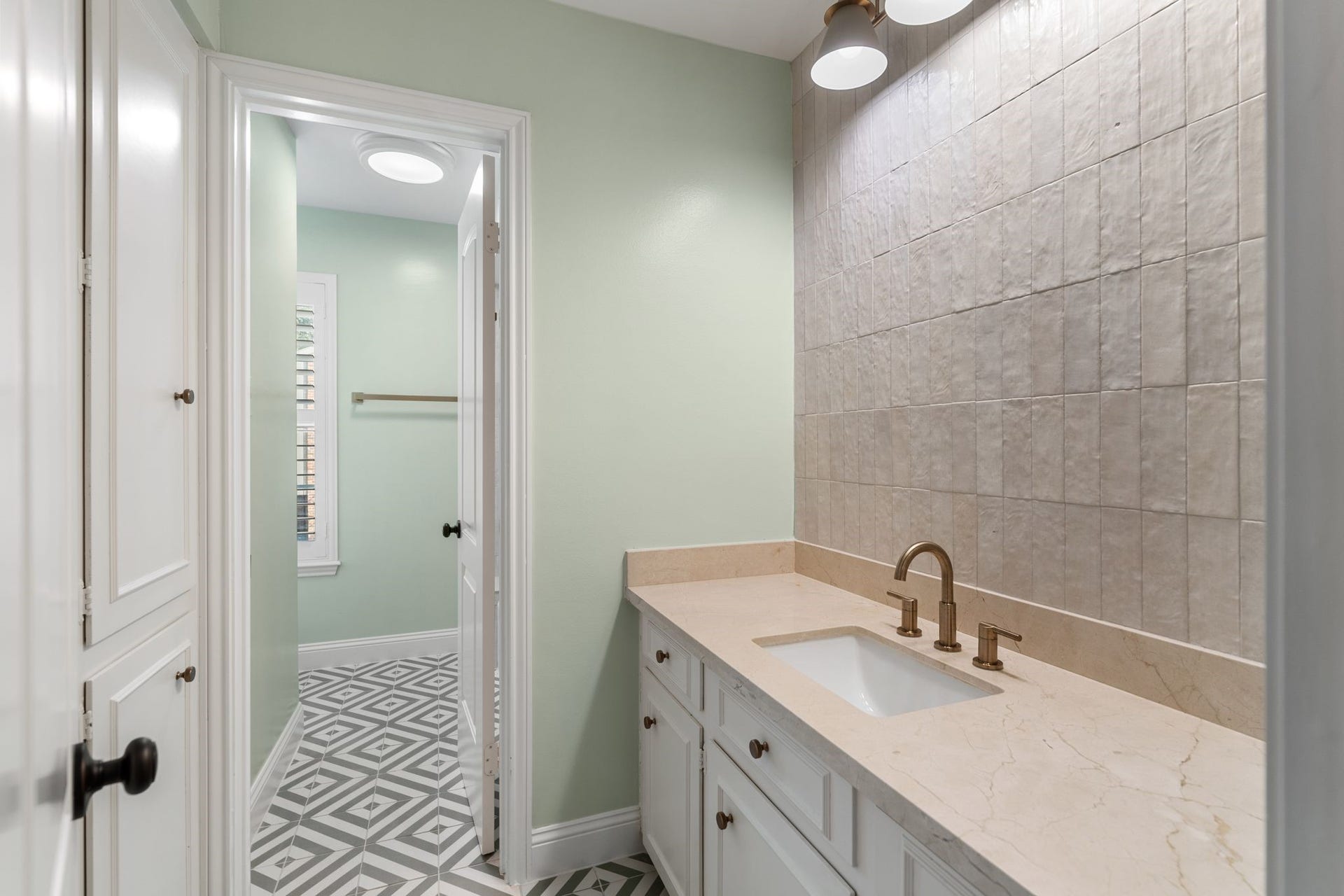 8619 La Fonte Street, Houston, TX 77024 Located just off the game room, this Hollywood bath features geometric patterned tile flooring, a white vanity with generous storage, a full-height tile accent wall and floor-to-ceiling built-in cabinetry. The separate water closet includes plantation shutters and a tub/shower combination with full-height tile surround, built-in niche and tiled ledge.