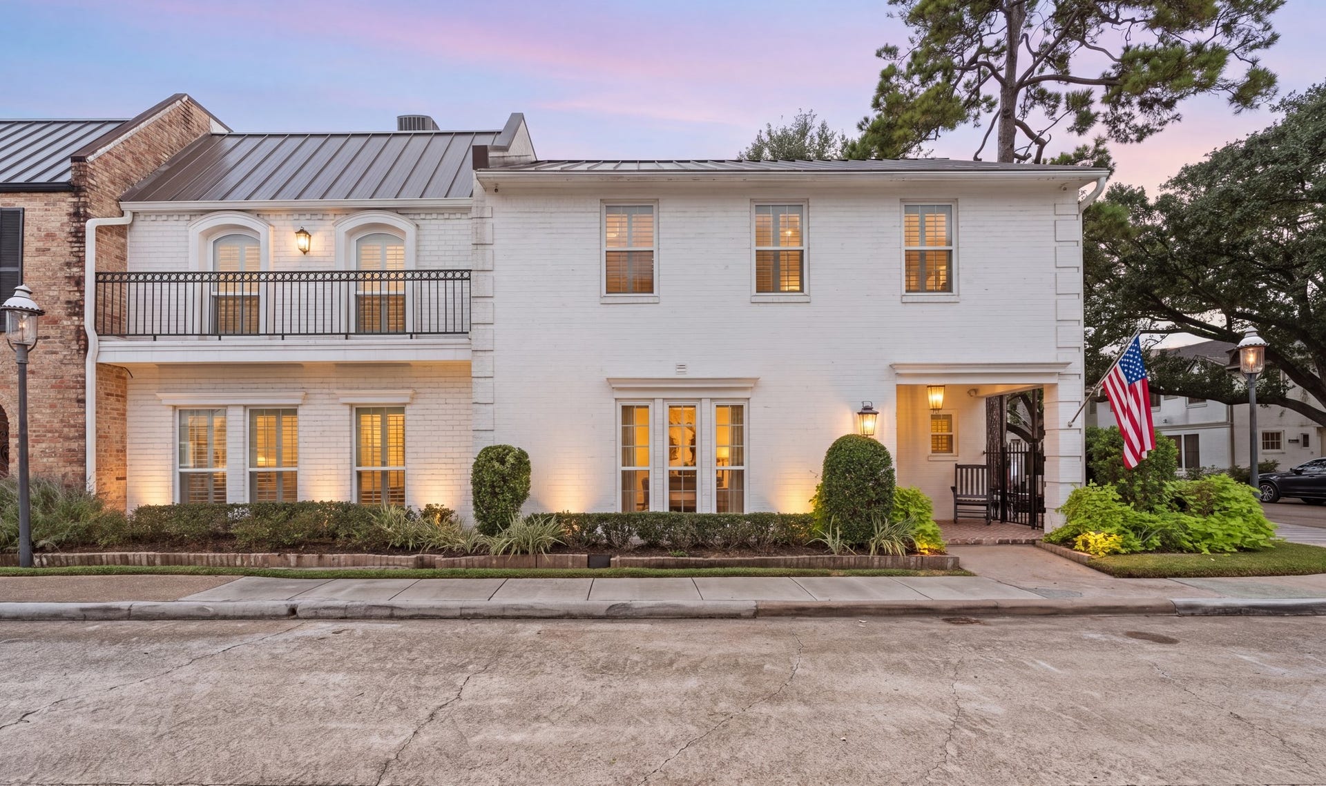 8619 La Fonte Street, Houston, TX 77024 A twilight view showcases the homes white brick exterior, metal roof and beautifully illuminated landscaping. Exterior lantern lighting and warm interior light create an inviting evening setting, while the corner location and mature trees complete the exterior.