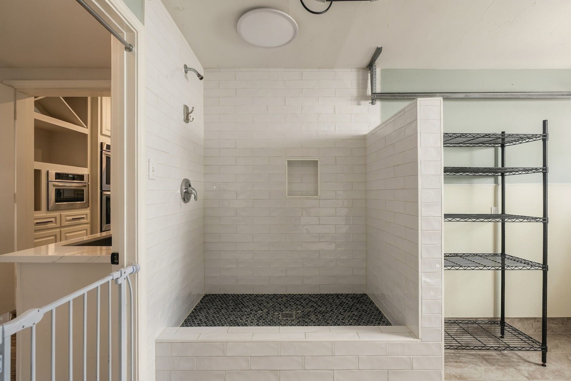 8619 La Fonte Street, Houston, TX 77024 The adjoining mudroom includes a dedicated dog washing station finished with a tiled surround, built-in niche and raised wash area, along with additional open shelving for everyday household or pet essentials. The space also provides direct garage access from the alley, creating a practical drop zone while helping keep the main utility room organized and functional.