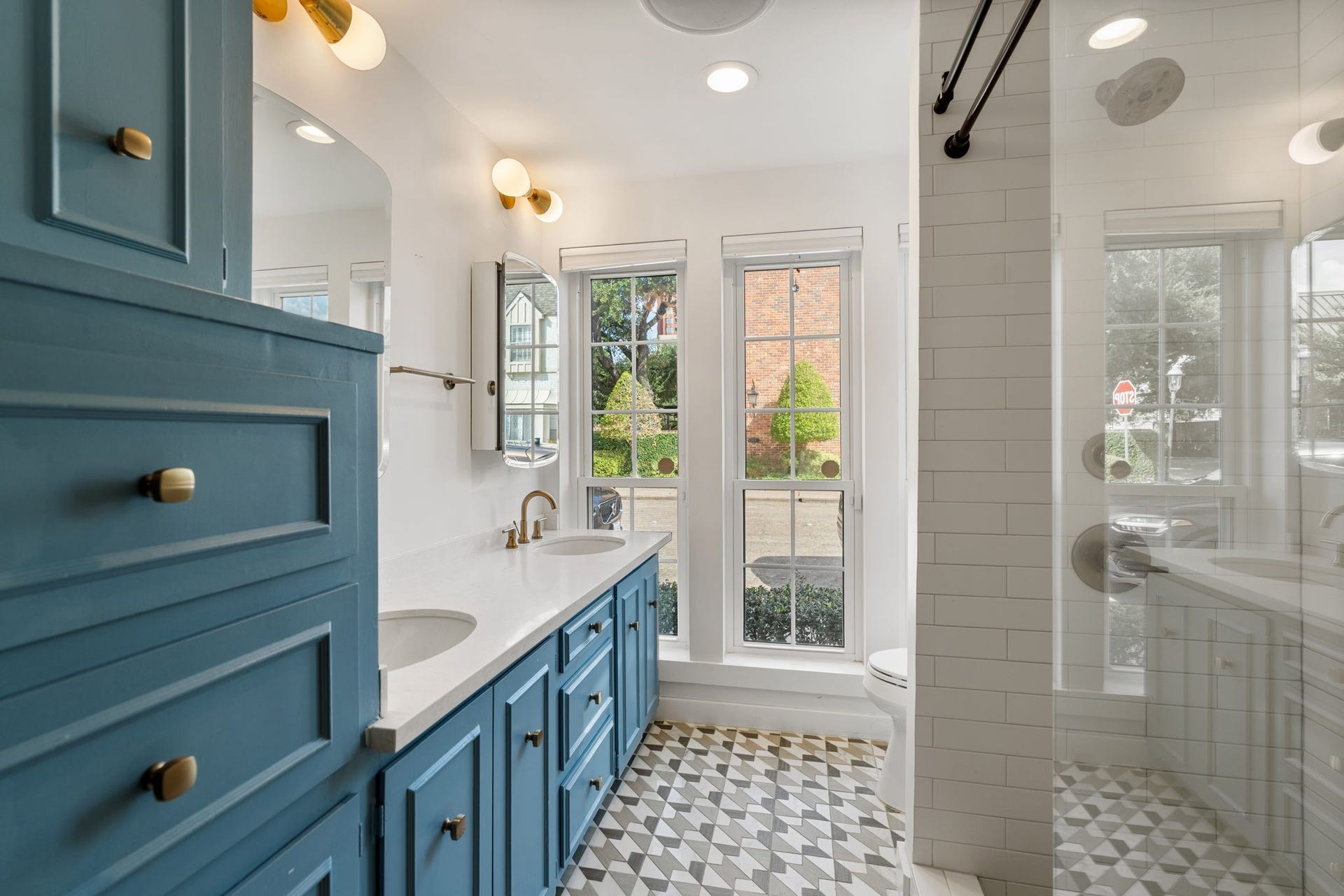 8619 La Fonte Street, Houston, TX 77024 The full ensuite bathroom off the media room features a double-sink vanity with quartz countertops, bold blue cabinetry, gold hardware and decorative gold vanity lights. Medicine cabinet mirrors provide additional storage, while three large windows with pull-down shades bring in plenty of natural light. The frameless glass shower is finished with white subway tile, a penny tile shower floor, built-in bench, handheld shower wand and built-in niche, while decorative tile flooring carries throughout the bathro
