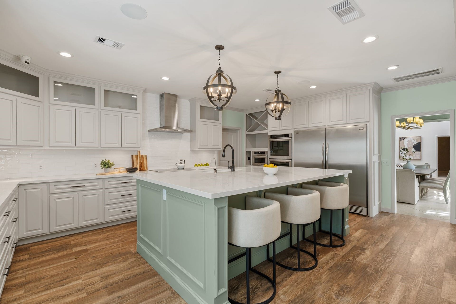 8619 La Fonte Street, Houston, TX 77024 A wider view showcases the kitchens two-tone cabinetry, spacious island and abundance of storage, including a full wall of cabinetry surrounding the appliance area. Matte black cabinet hardware adds contrast against the white cabinetry, while under-cabinet lighting illuminates the quartz countertops and subway tile backsplash. The electric cooktop with stainless steel vent hood is positioned along the perimeter, leaving the oversized island open for prep, serving and breakfast bar seating.