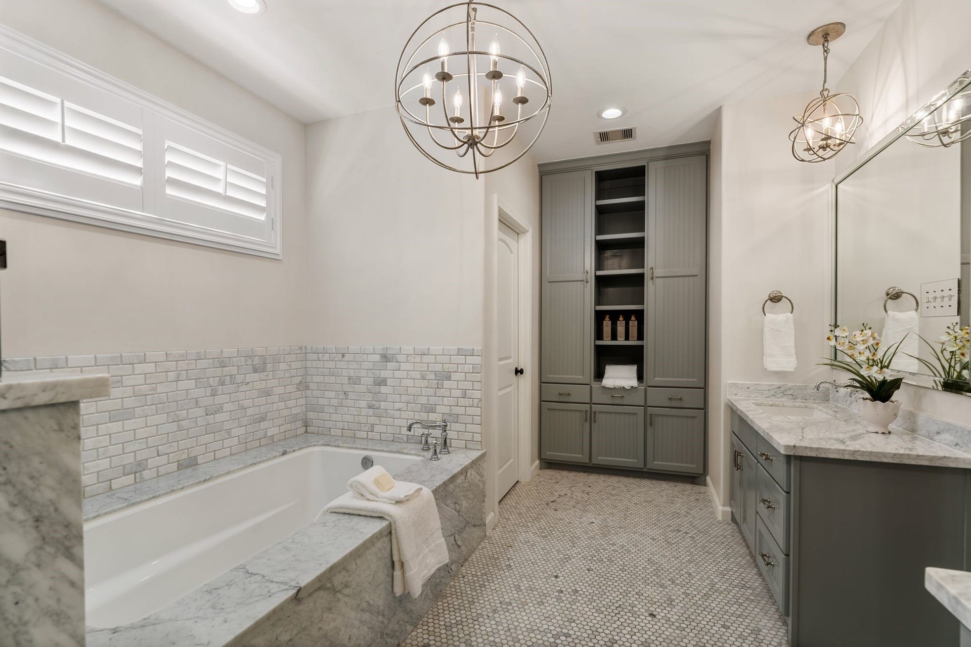 8619 La Fonte Street, Houston, TX 77024 This view showcases the separate soaking tub wrapped in marble with a coordinating marble surround and marble wainscoting along the wall. Windows with plantation shutters bring in natural light above the tub, while floor-to-ceiling linen and storage cabinetry provides extensive organization with drawers, cabinets and open shelving. The bathroom also includes a separate room for the water closet.