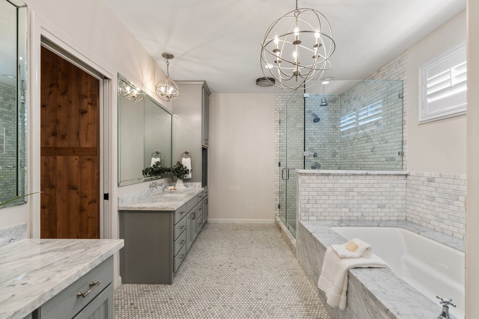 8619 La Fonte Street, Houston, TX 77024 The primary bathroom features two vanities with marble countertops, gray cabinetry and coordinating polished nickel/chrome hardware and fixtures. An oversized framed mirror spans the main vanity, while marble penny tile flooring carries throughout the space. A large frameless glass walk-in shower includes a rain shower head, an additional wall-mounted shower head and a built-in bench, with decorative pendant lighting and recessed lighting overhead.
