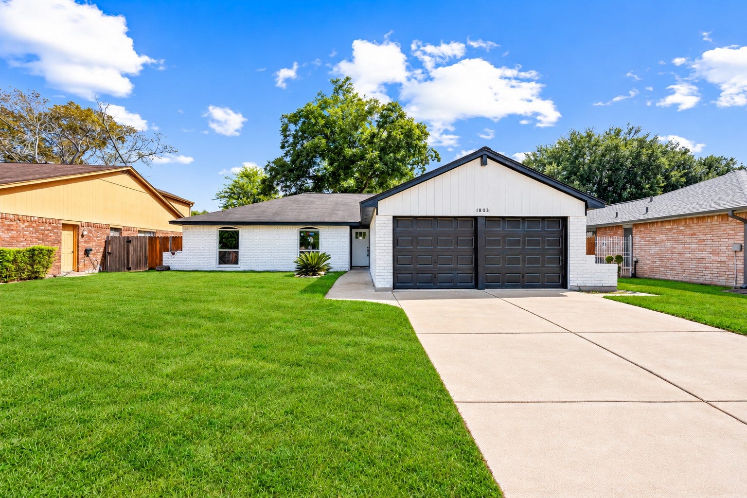 1803 Thornbrook Drive, Missouri City, TX 77489 Charming single-story home featuring a clean white brick exterior, bold dark garage doors, and a spacious driveway with a two-car garage.