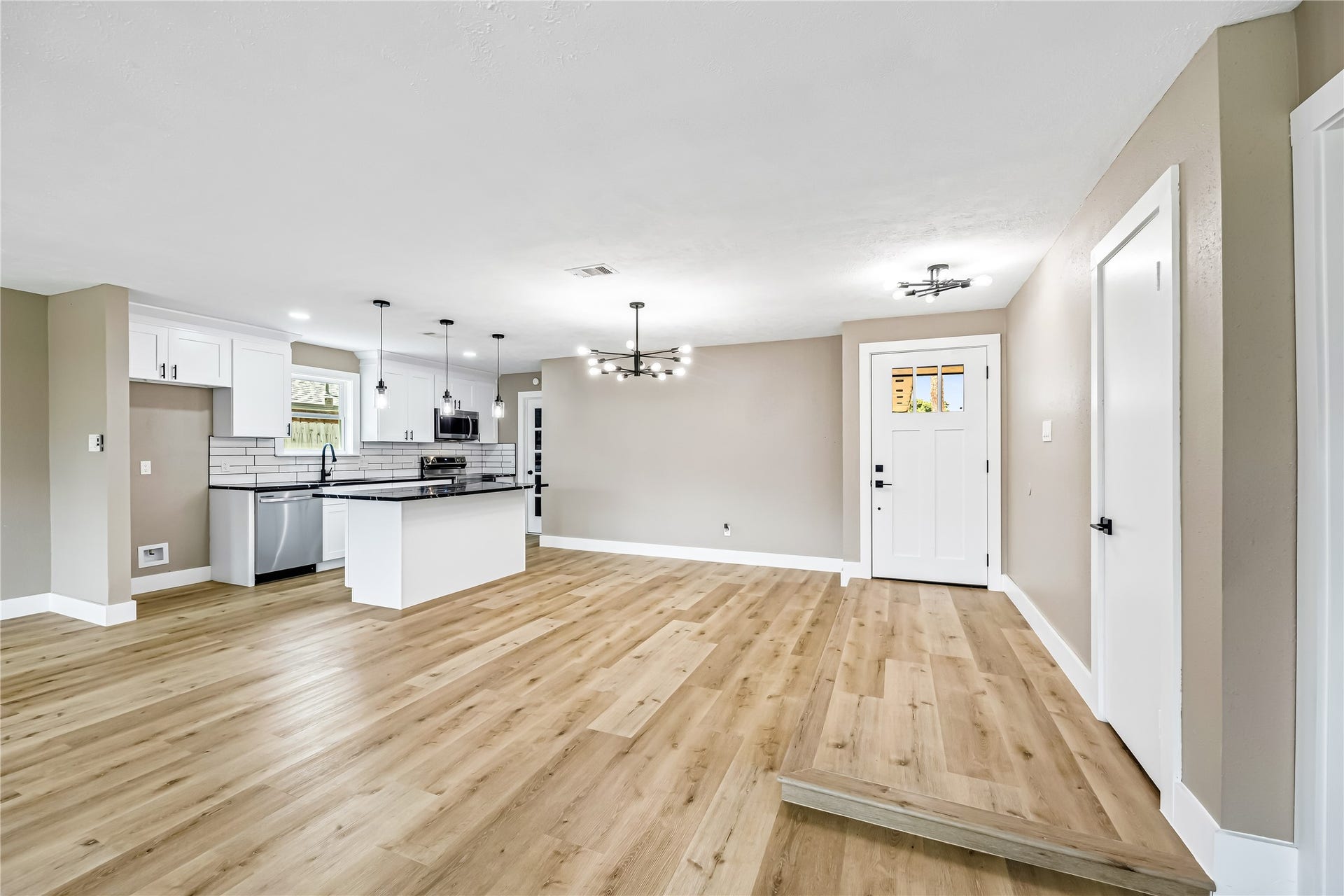 1803 Thornbrook Drive, Missouri City, TX 77489 Spacious open-concept interior featuring warm wood-look flooring, a modern kitchen with white cabinetry and dark countertops, stylish statement lighting, and clean neutral finishes. The wide layout offers plenty of flexibility for dining, entertaining, and everyday living.