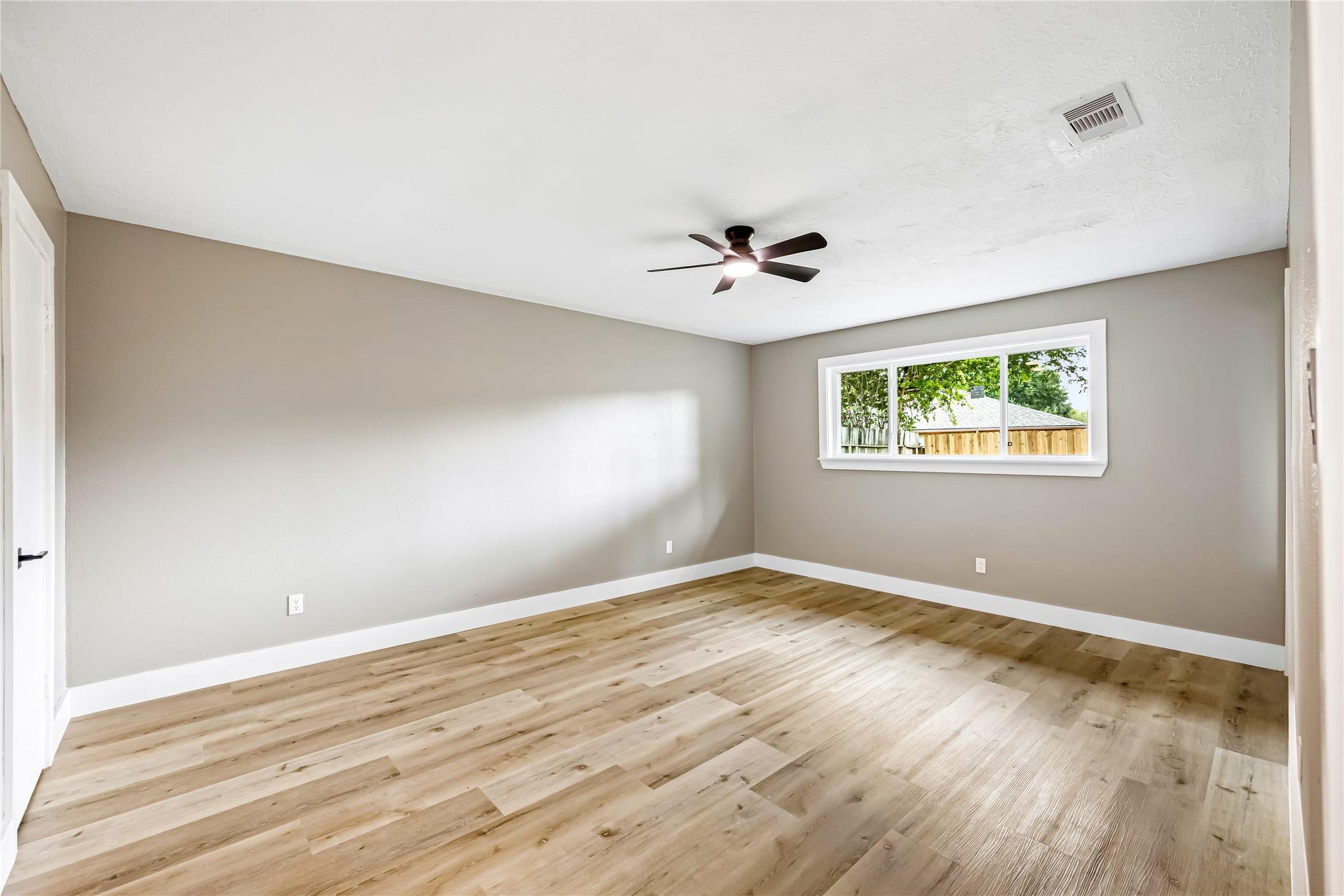 1803 Thornbrook Drive, Missouri City, TX 77489 Spacious bedroom featuring warm wood-look flooring, neutral walls, a modern ceiling fan, and a wide window that brings in plenty of natural light.