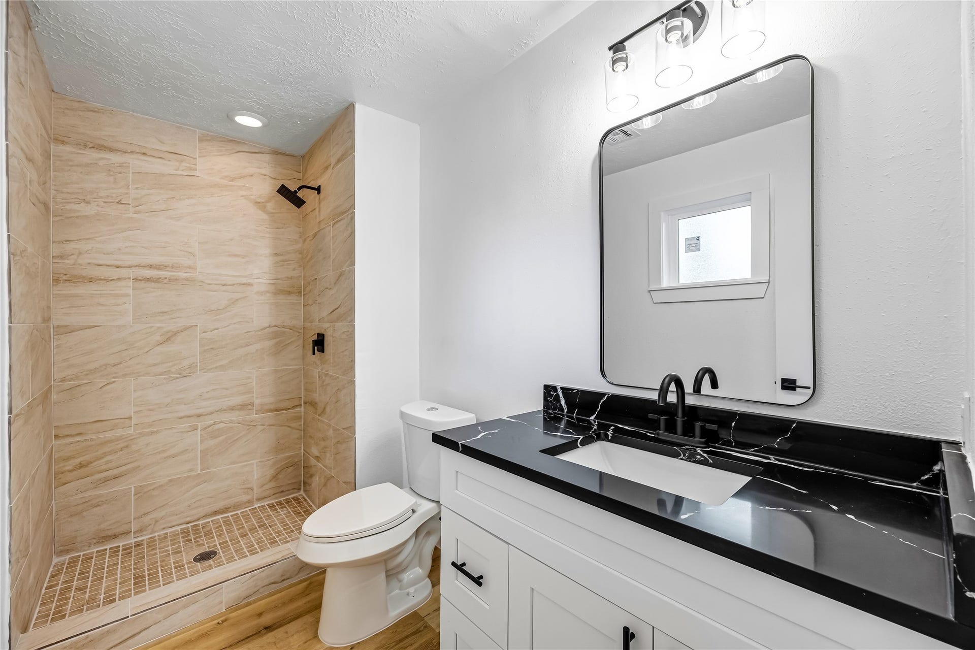 1803 Thornbrook Drive, Missouri City, TX 77489 Updated bathroom featuring a walk-in tiled shower, modern white vanity, bold black stone-look countertop, matte black fixtures, and a large framed mirror.