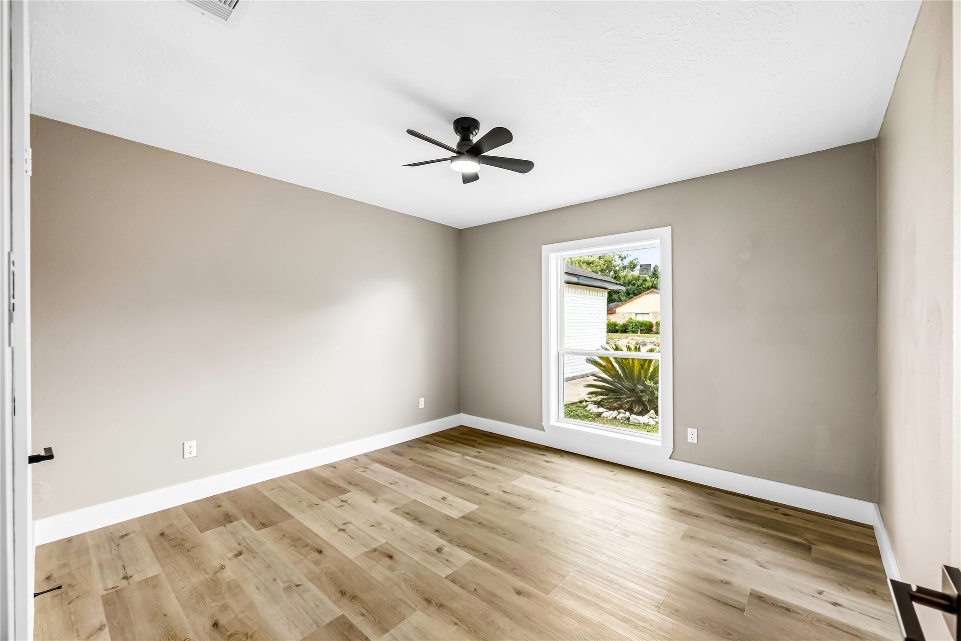 1803 Thornbrook Drive, Missouri City, TX 77489 Bright and inviting bedroom featuring warm wood-look flooring, soft neutral walls, crisp white trim, and a modern ceiling fan.