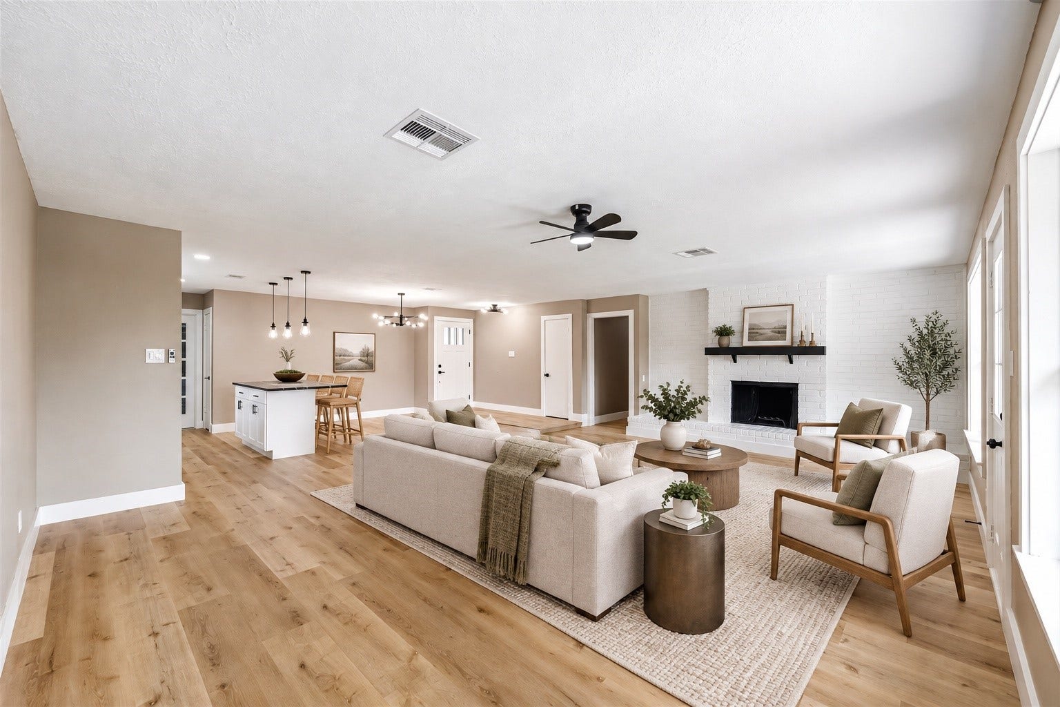 1803 Thornbrook Drive, Missouri City, TX 77489 Spacious open-concept living area featuring warm wood-look flooring, a white brick fireplace, modern ceiling fan, and abundant natural light. The seamless connection to the kitchen and dining area creates an inviting layout with plenty of room for relaxing, entertaining, and everyday living.