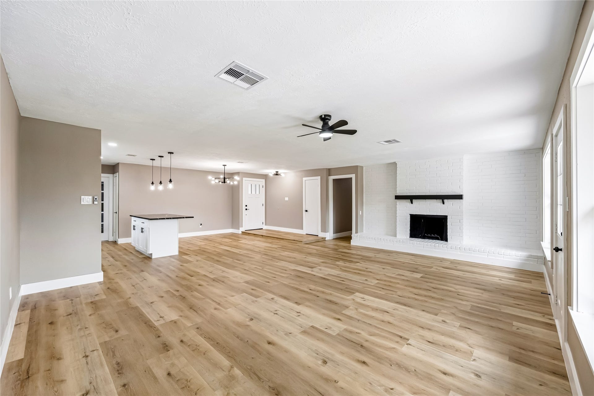 1803 Thornbrook Drive, Missouri City, TX 77489 Spacious open-concept living area featuring warm wood-look flooring, a striking white brick fireplace, modern lighting, and a large kitchen island. The expansive layout offers plenty of room for flexible living and dining arrangements, with abundant natural light creating a bright and welcoming atmosphere.