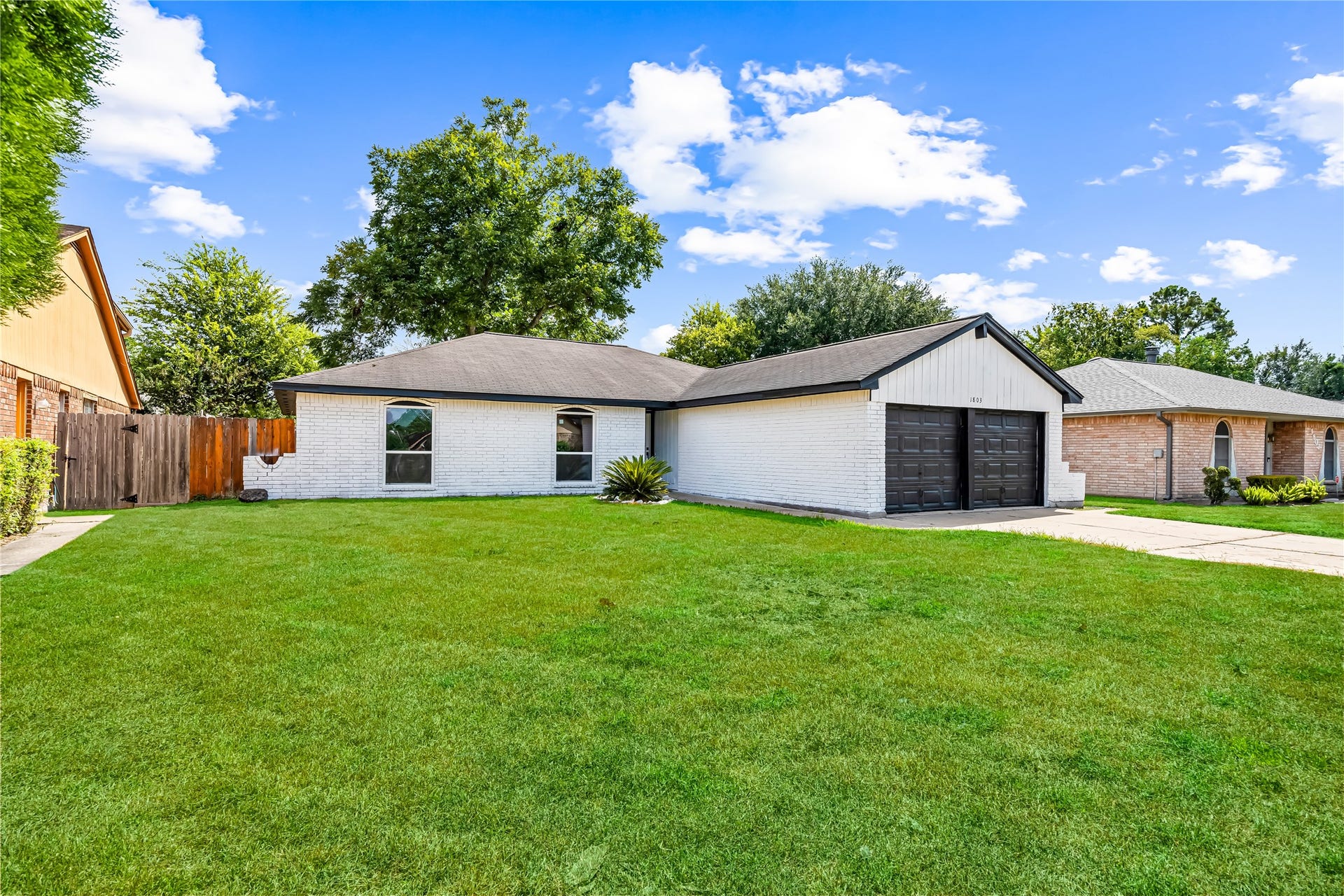 1803 Thornbrook Drive, Missouri City, TX 77489 Inviting single-story home featuring a bright white brick exterior, dark garage doors, and a wide front yard that gives the property a spacious feel. The clean modern contrast and broad frontage create strong curb appeal and a welcoming first impression.