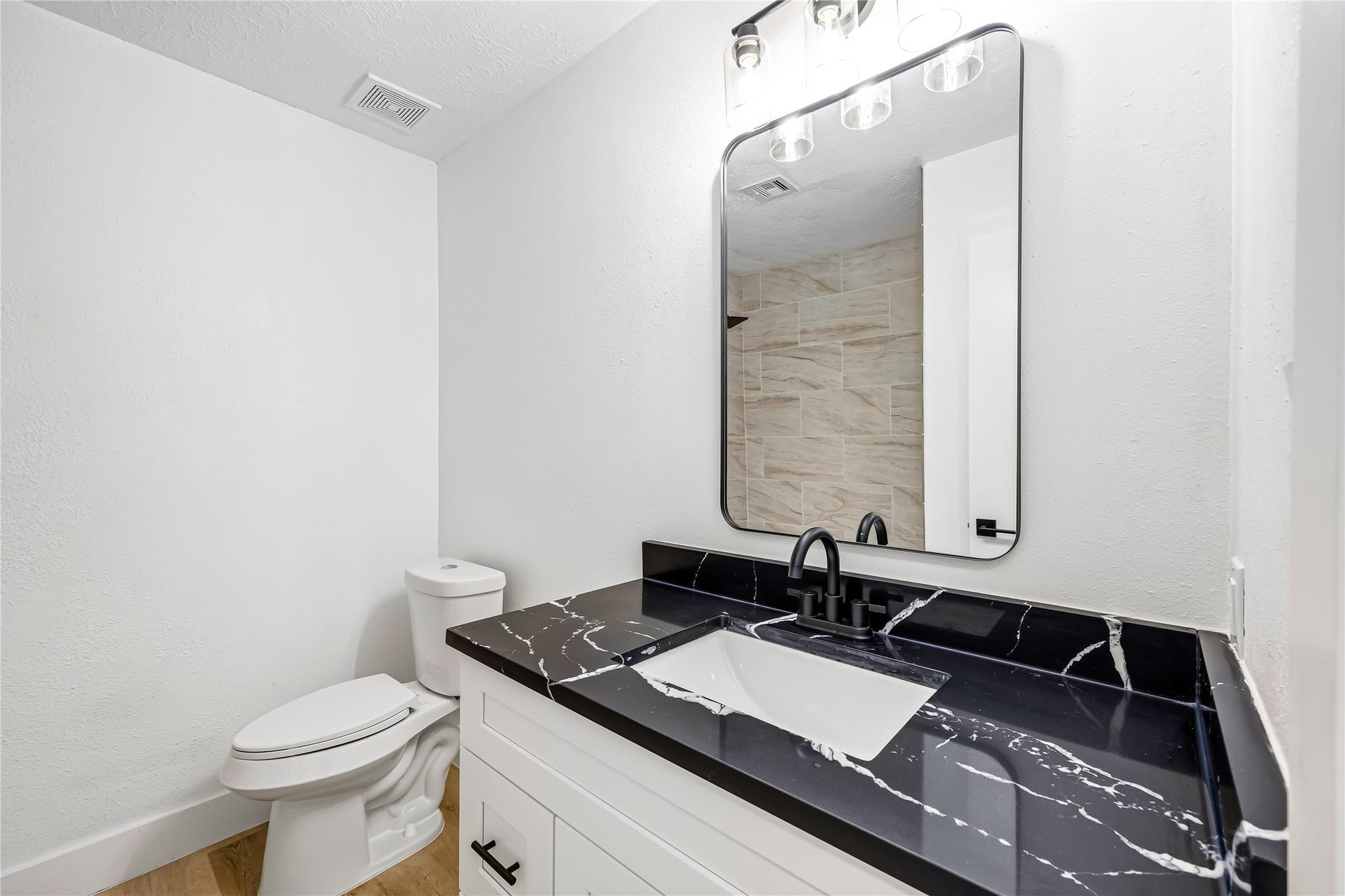 1803 Thornbrook Drive, Missouri City, TX 77489 Updated bathroom featuring a white vanity with bold black stone-look countertop, matte black fixtures, an arched mirror, and modern vanity lighting. The clean neutral finishes and tiled shower detail create a stylish, polished, and contemporary space.