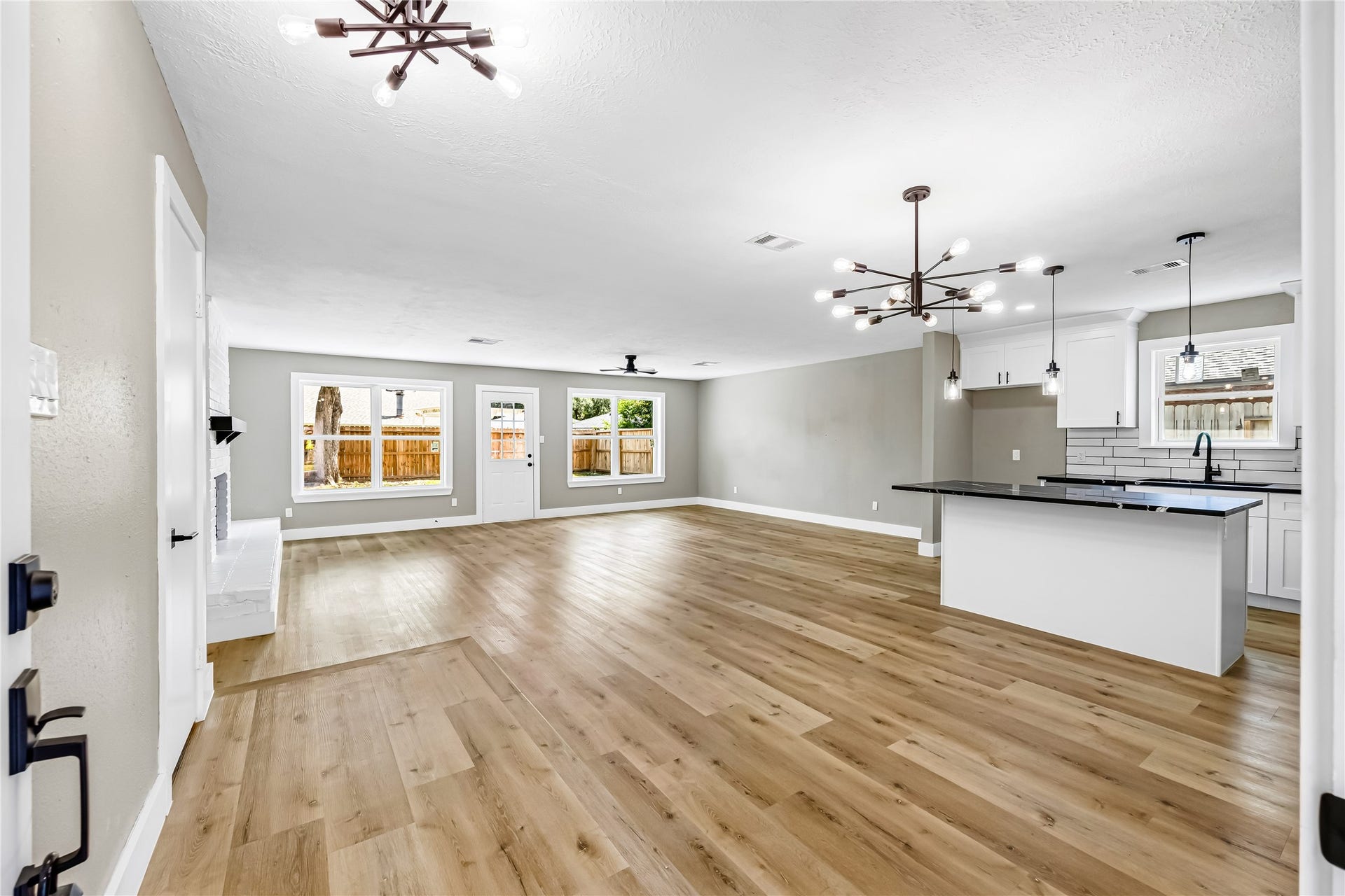 1803 Thornbrook Drive, Missouri City, TX 77489 Spacious open-concept living and kitchen area featuring warm wood-look flooring, modern statement lighting, a large island, white cabinetry, and sleek black accents. The wide-open layout offers excellent flexibility for both living and dining while large windows bring in plenty of natural light.