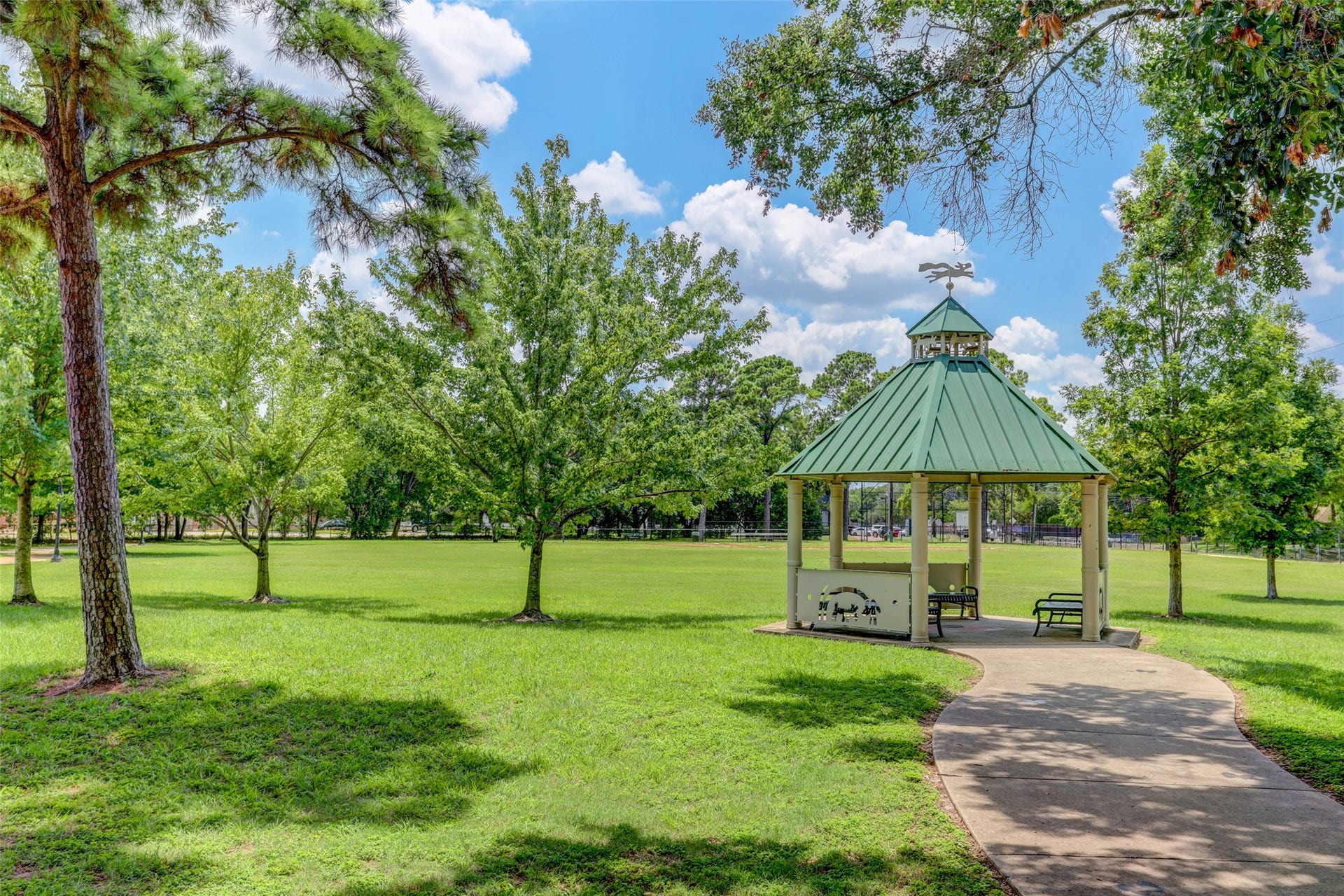Charming gazebo set in a lush green park, surrounded by mature trees and a winding pathway.