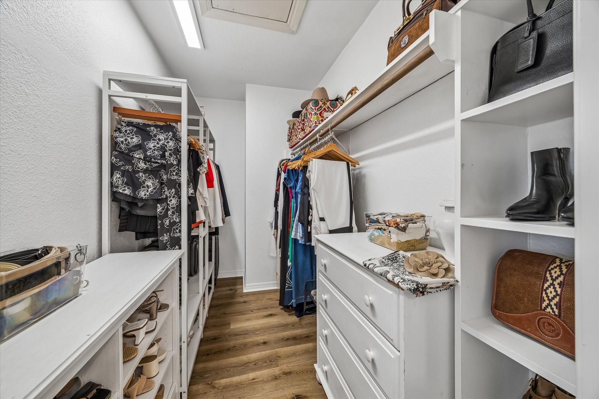 Spacious walk-in closet featuring custom shelving, ample hanging space, and elegant wood flooring.