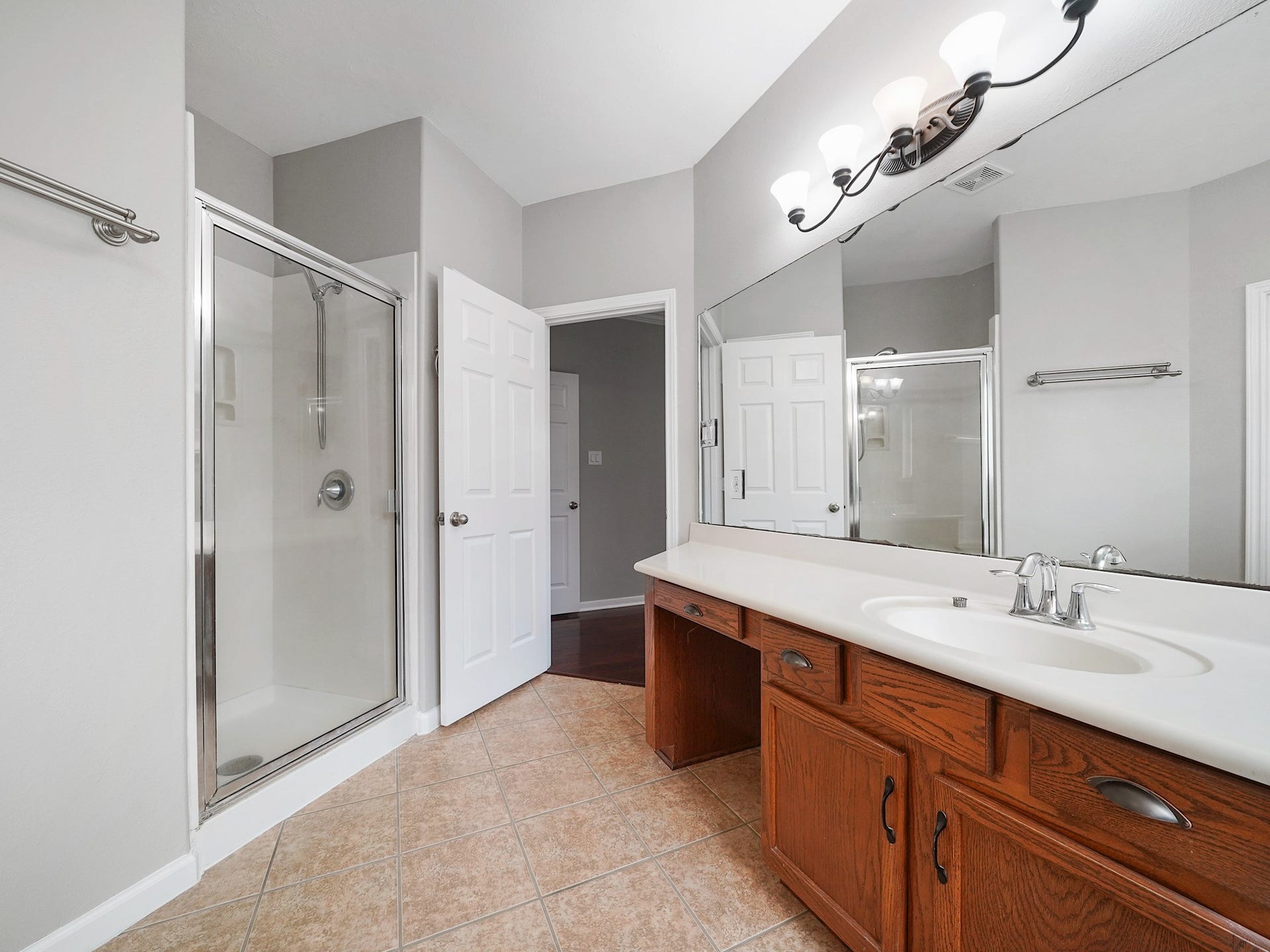 A second view reveals the spacious primary bath, featuring a glass-enclosed shower, long vanity, and abundant storage.