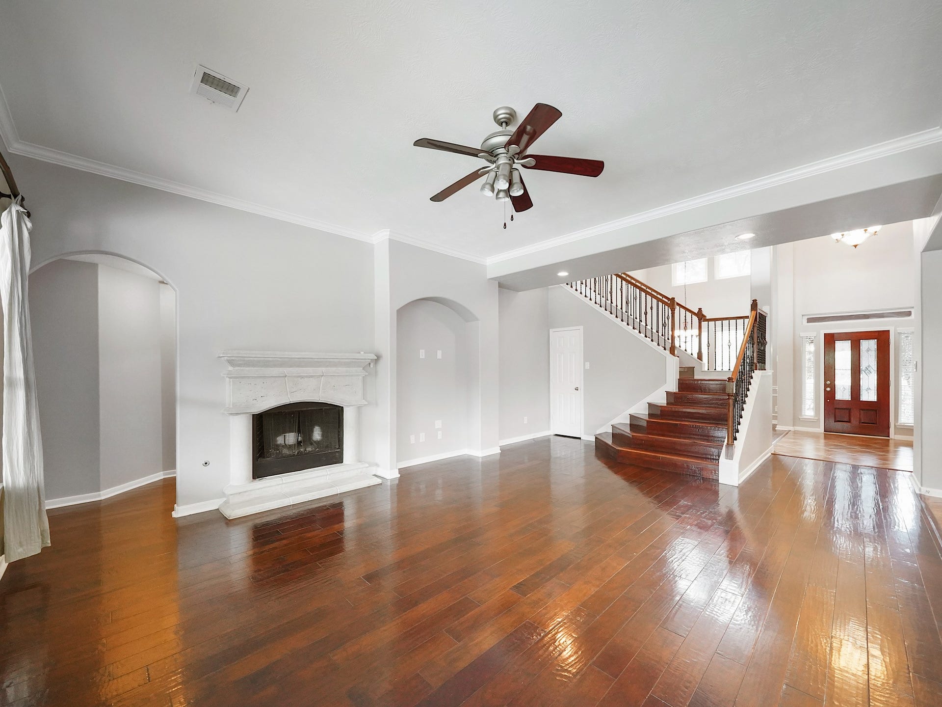 A wide view showcases the fireplace, arched passageways, and open connection between the living room, staircase, and entry.