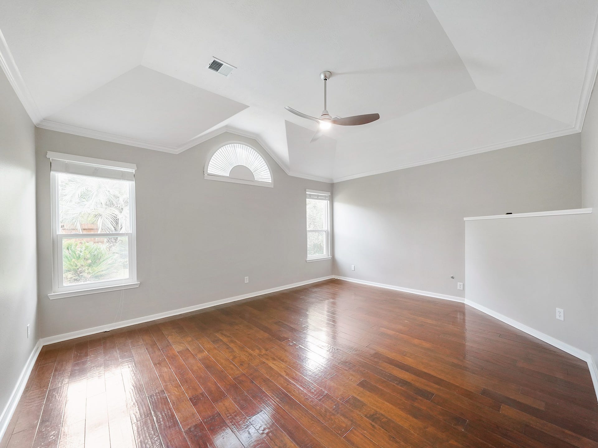 A vaulted ceiling, architectural angles, and an arched transom window give the primary suite a memorable sense of scale and natural light.