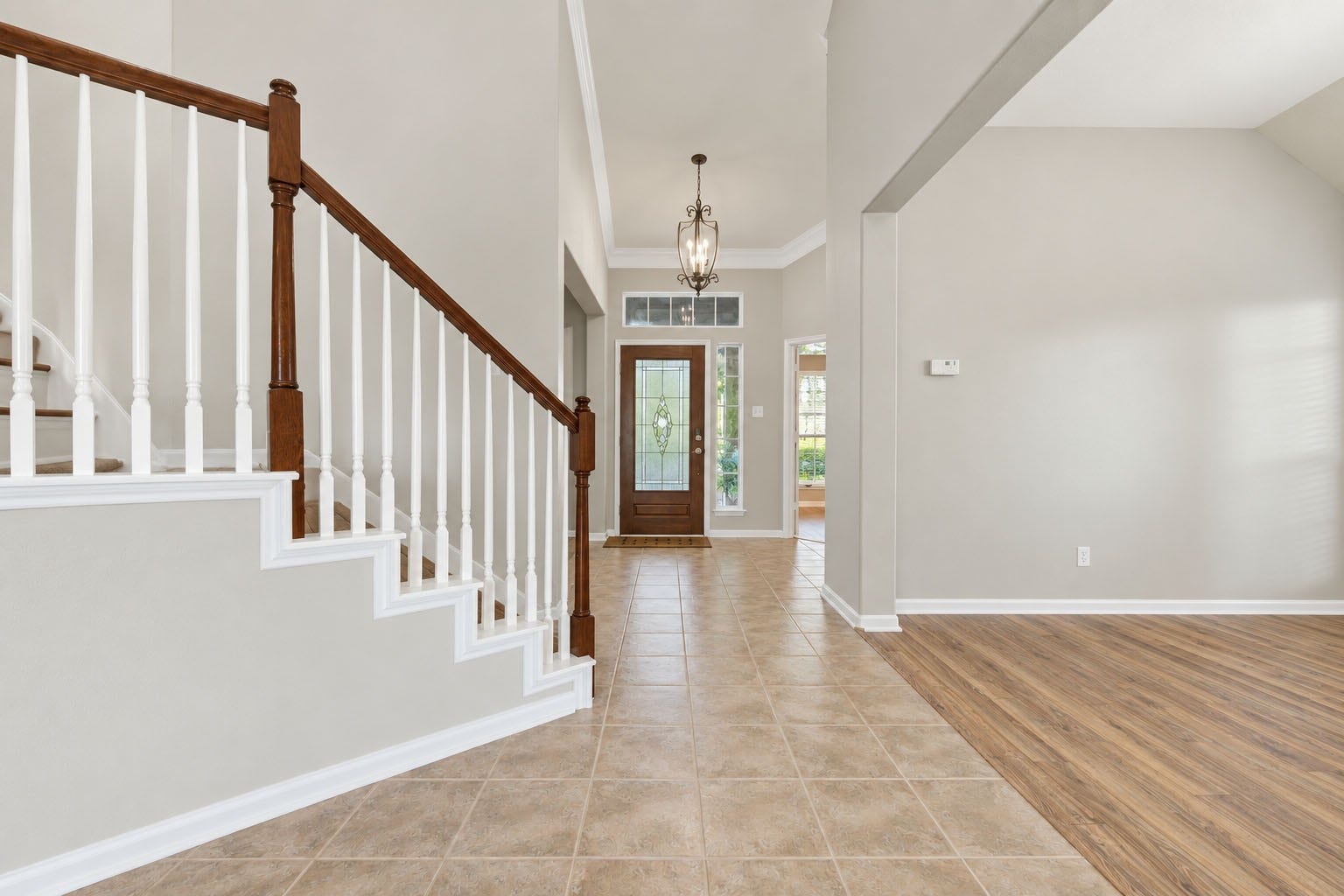 Welcoming two-story entry featuring a decorative glass front door, high ceilings, elegant light fixture, and staircase with wood accents. The open layout provides a view into the adjacent flex/bonus room.