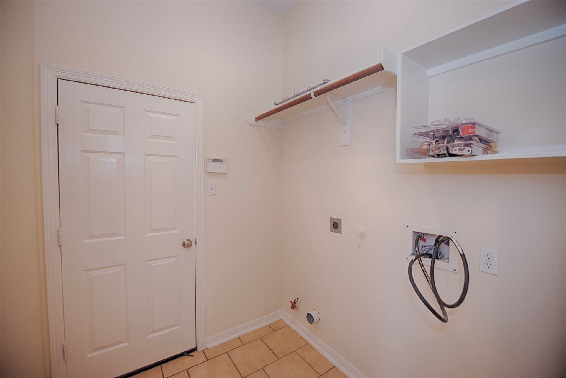 Utility room with door to the garage. There is built in shelving for your laundry essentials and hanging rod for hanging your clothes as you remove from the dryer.