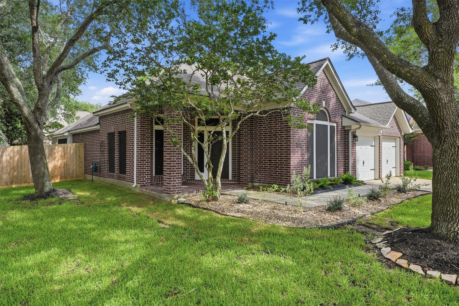 Side angle highlighting the covered front porch area, mature shade trees, and privacy fencing.