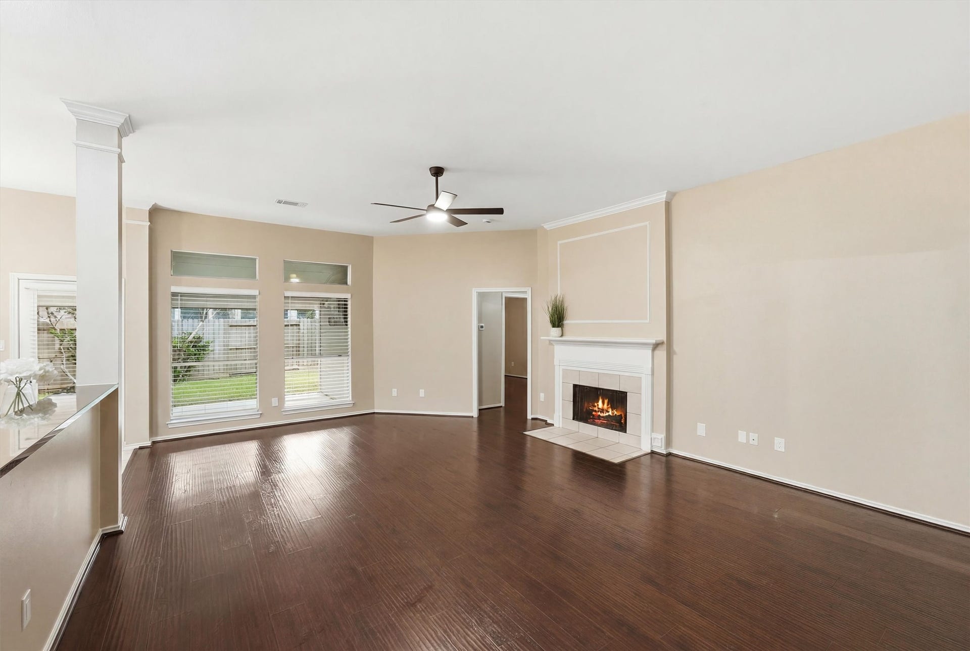 Expansive living area boasting rich hardwood-style flooring, a central ceiling fan, and a cozy tile-surround fireplace.