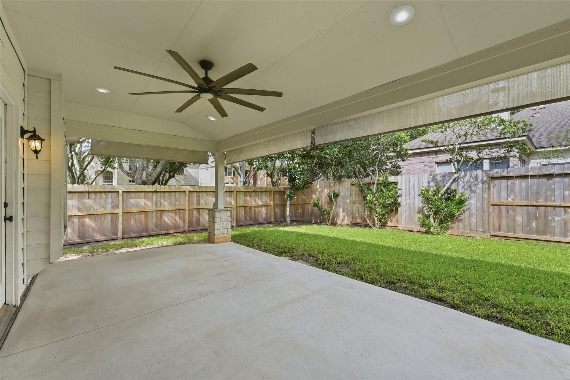 Another view of the generous outdoor living space showcasing stone-wrapped support columns and a clear view of the private, fully fenced grassy backyard.