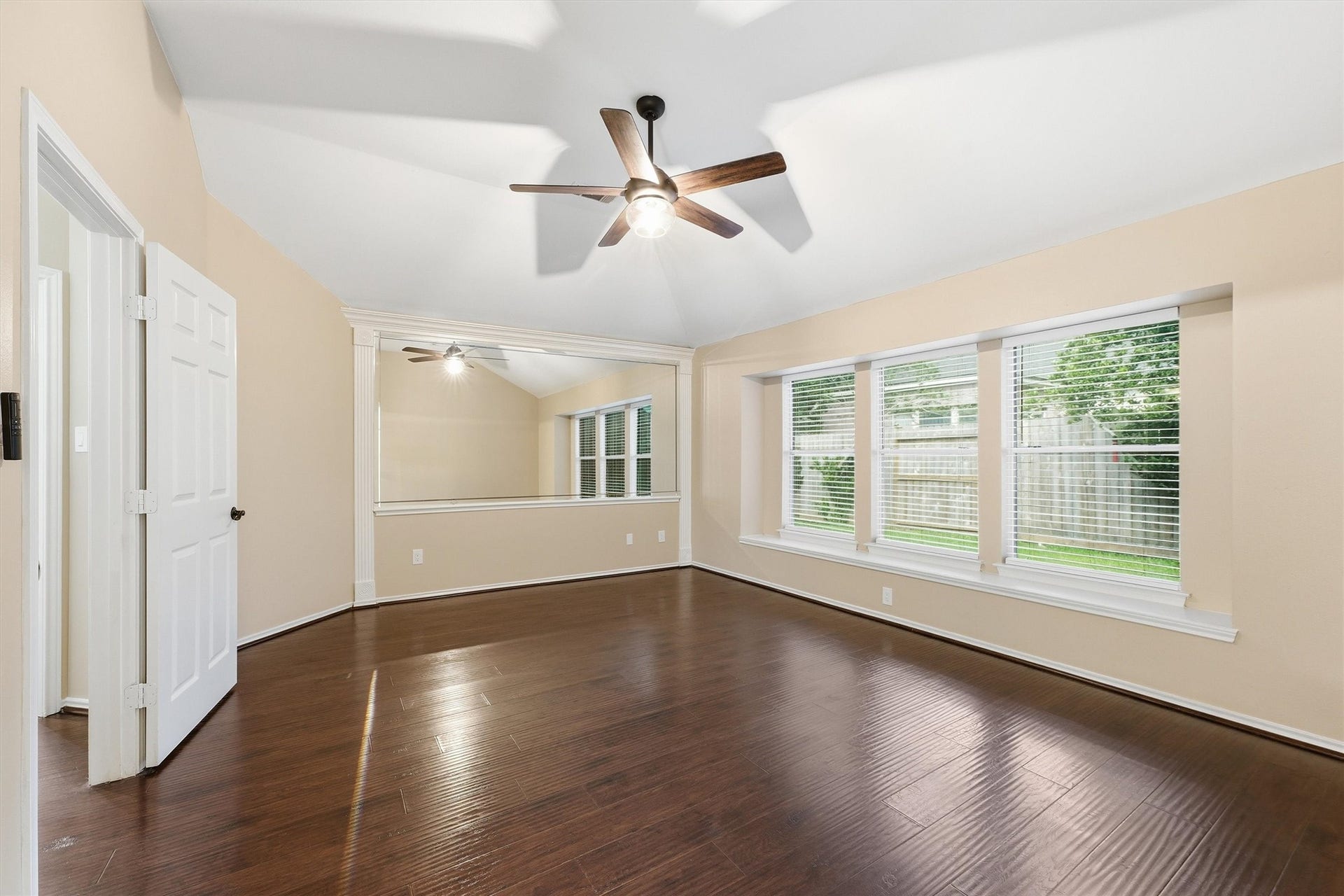 Generous primary suite boasting elegant vaulted ceilings, a large framed accent mirror, rich hardwood flooring, and expansive windows offering abundant natural light.