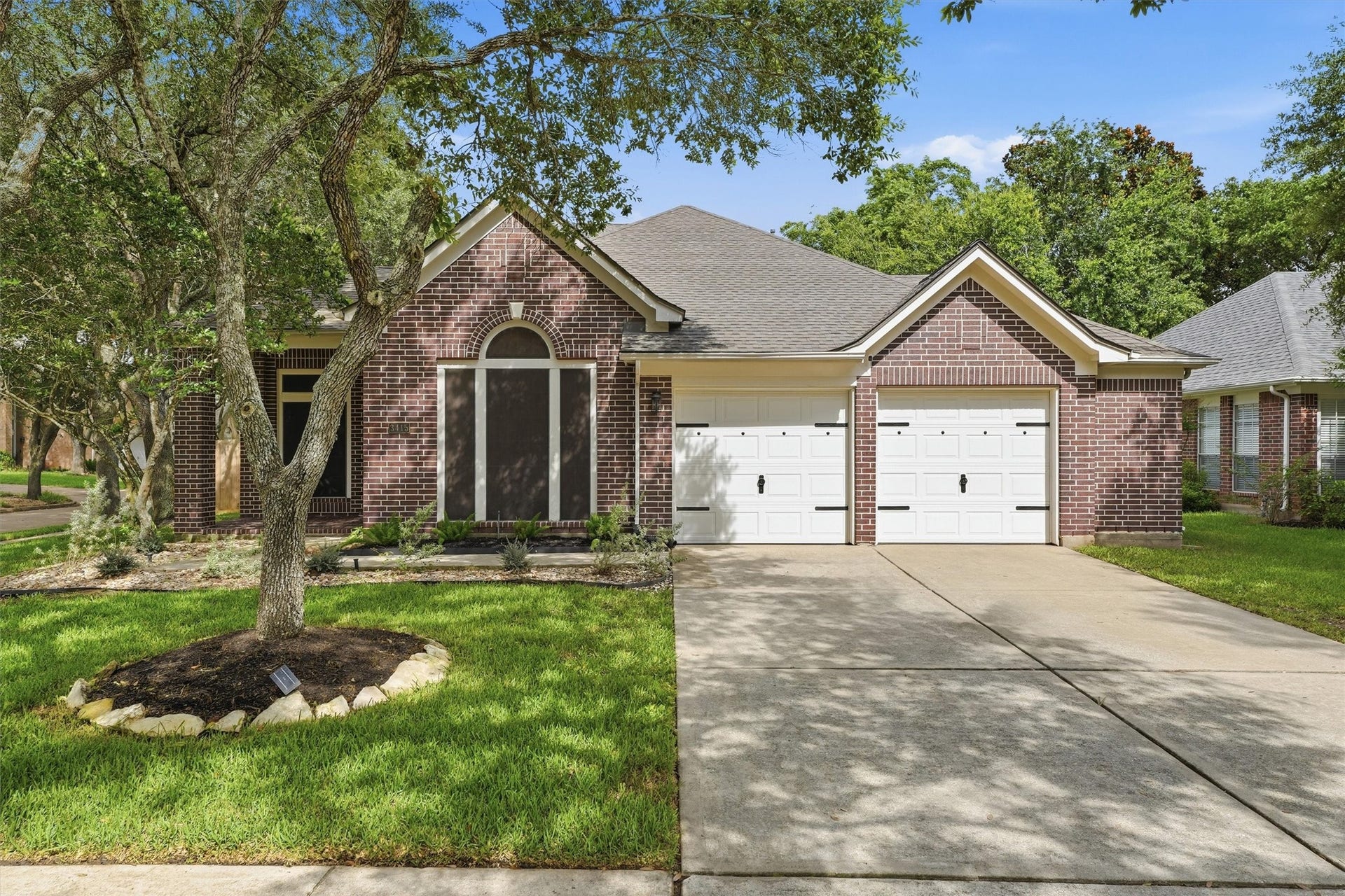 Front exterior featuring classic brick architecture, a manicured lawn, mature trees, and a two-car garage.