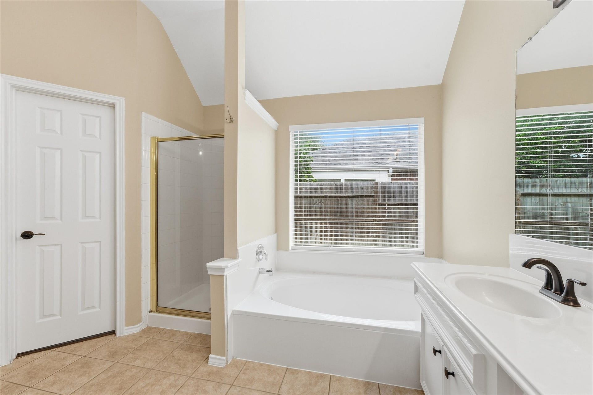 Primary bath retreat showcases a deep soaking tub positioned under a bright window, a separate glass-enclosed shower, and a clean ceramic tile floor.
