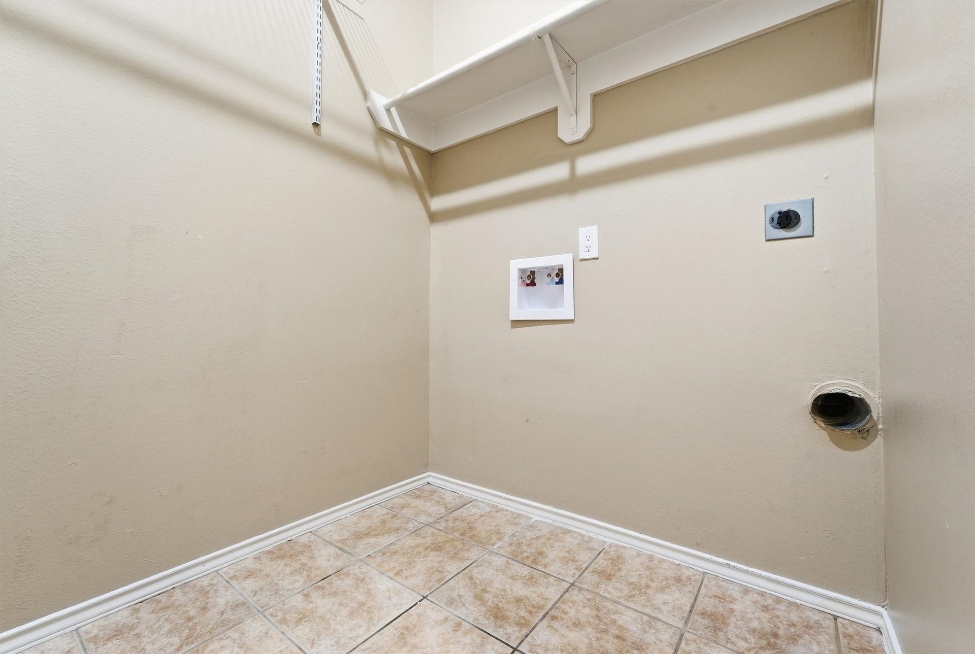 Convenient in-house laundry room equipped with built-in overhead storage shelving, tile flooring, and standard washer/dryer hookups.