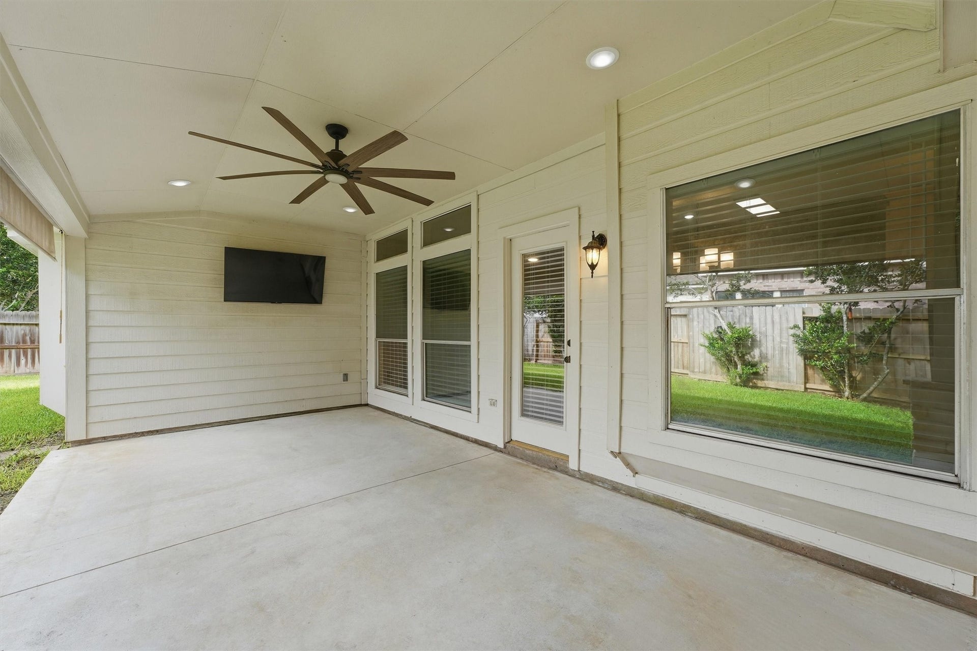 Massive covered back patio equipped with a premium multi-blade ceiling fan, recessed lighting, a mounted TV setup, and pull-down sun shades for year-round comfort.
