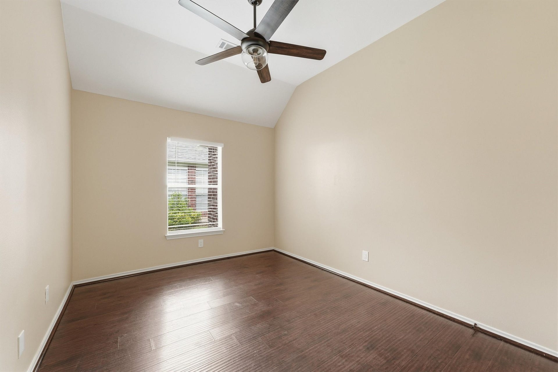 Spacious secondary bedroom showcasing impressive vaulted ceilings, a wide multi-blade ceiling fan, neutral paint, and pristine hardwood floors.