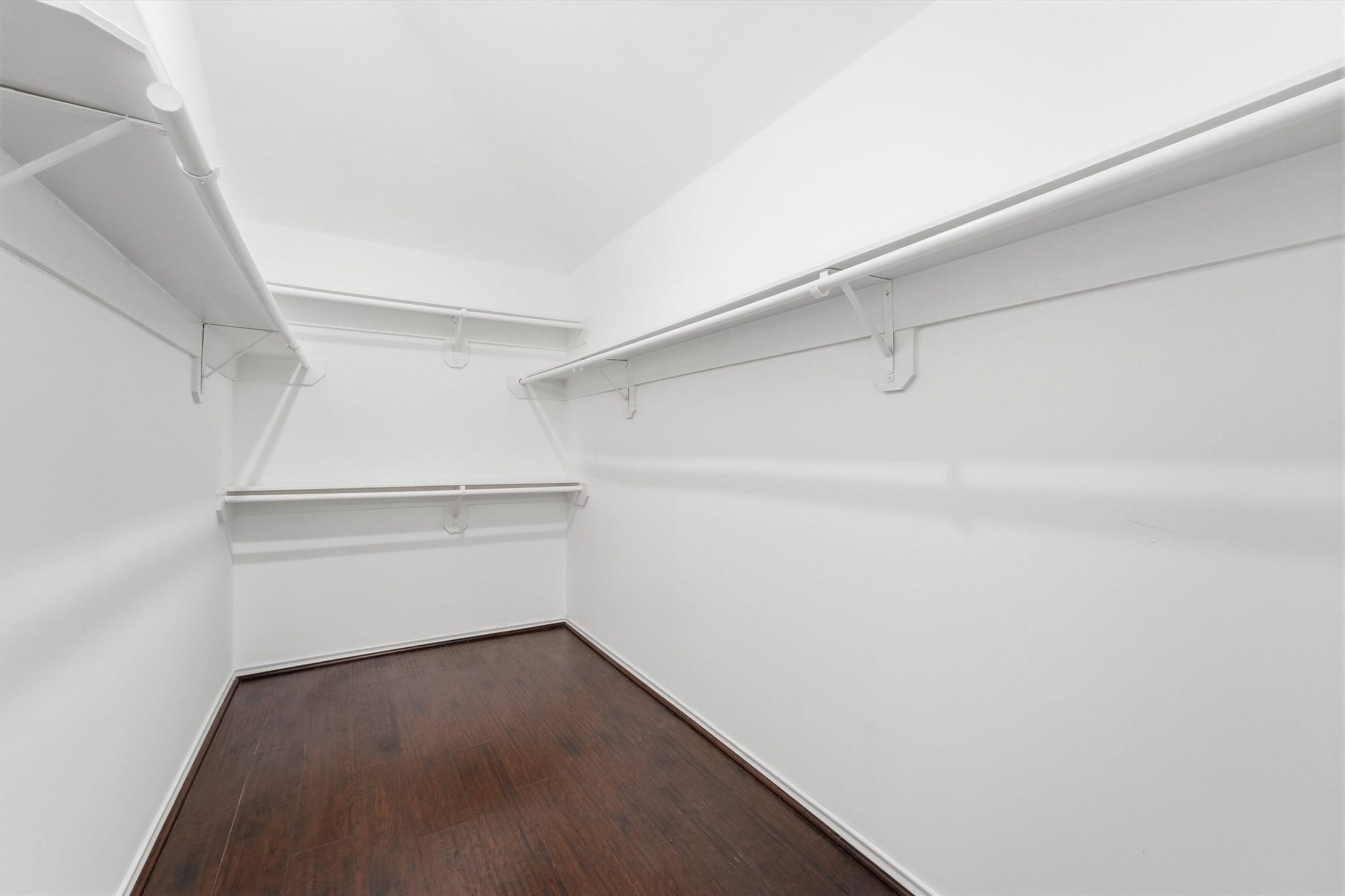 Expansive primary walk-in closet featuring multi-level wrap-around hanging rods, built-in storage shelving, and continuous engineered hardwood flooring.