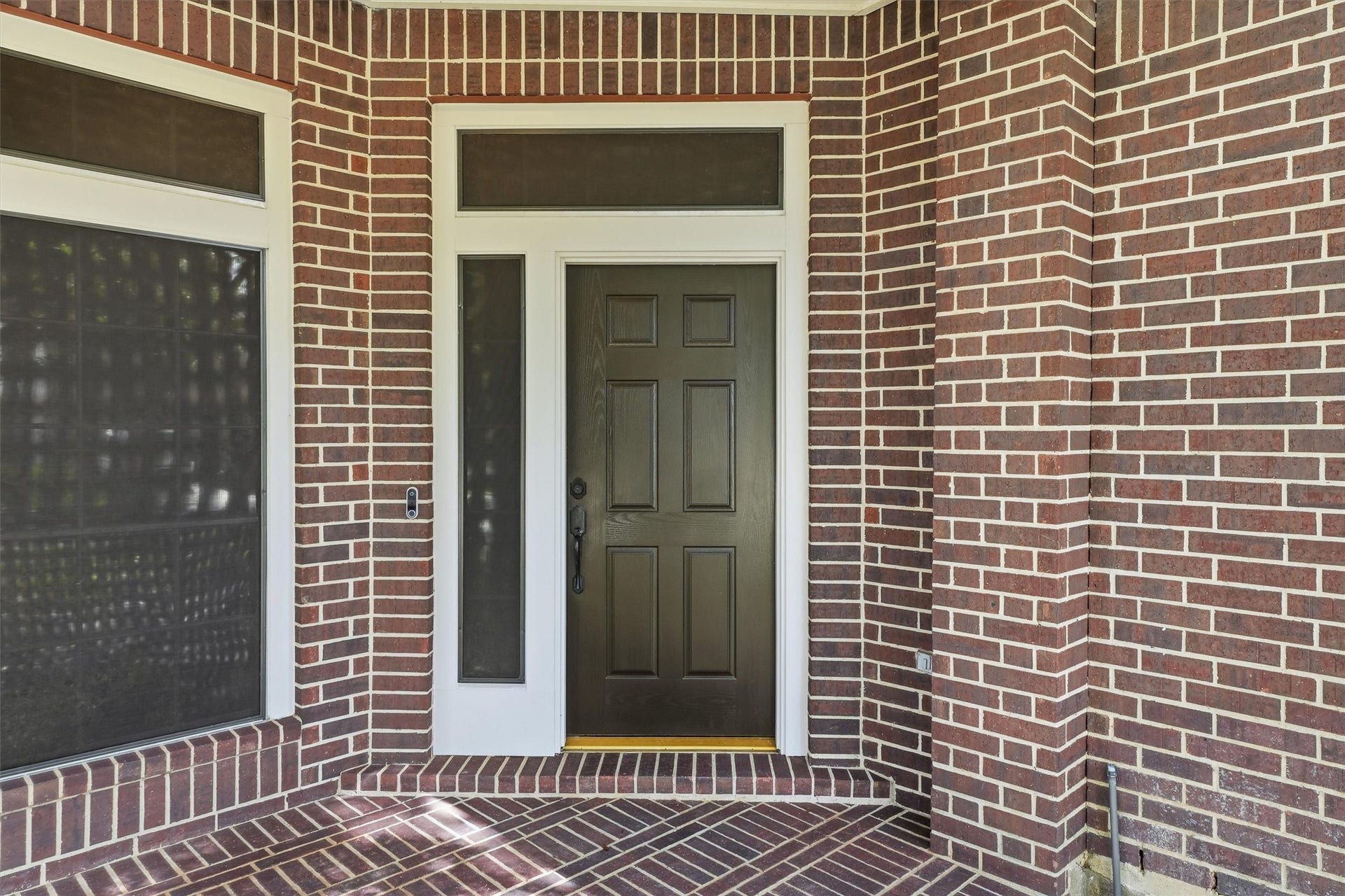Covered front entry with herringbone brick flooring, a classic six-panel door, and a sidelight window.